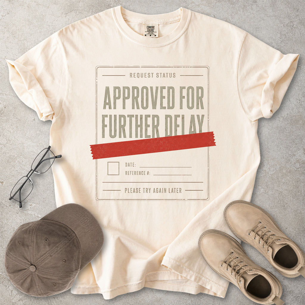 Ivory beige Comfort Colors 1717 T-shirt with a funny Approved for Further Delay graphic showing a request status form covered with red tape.