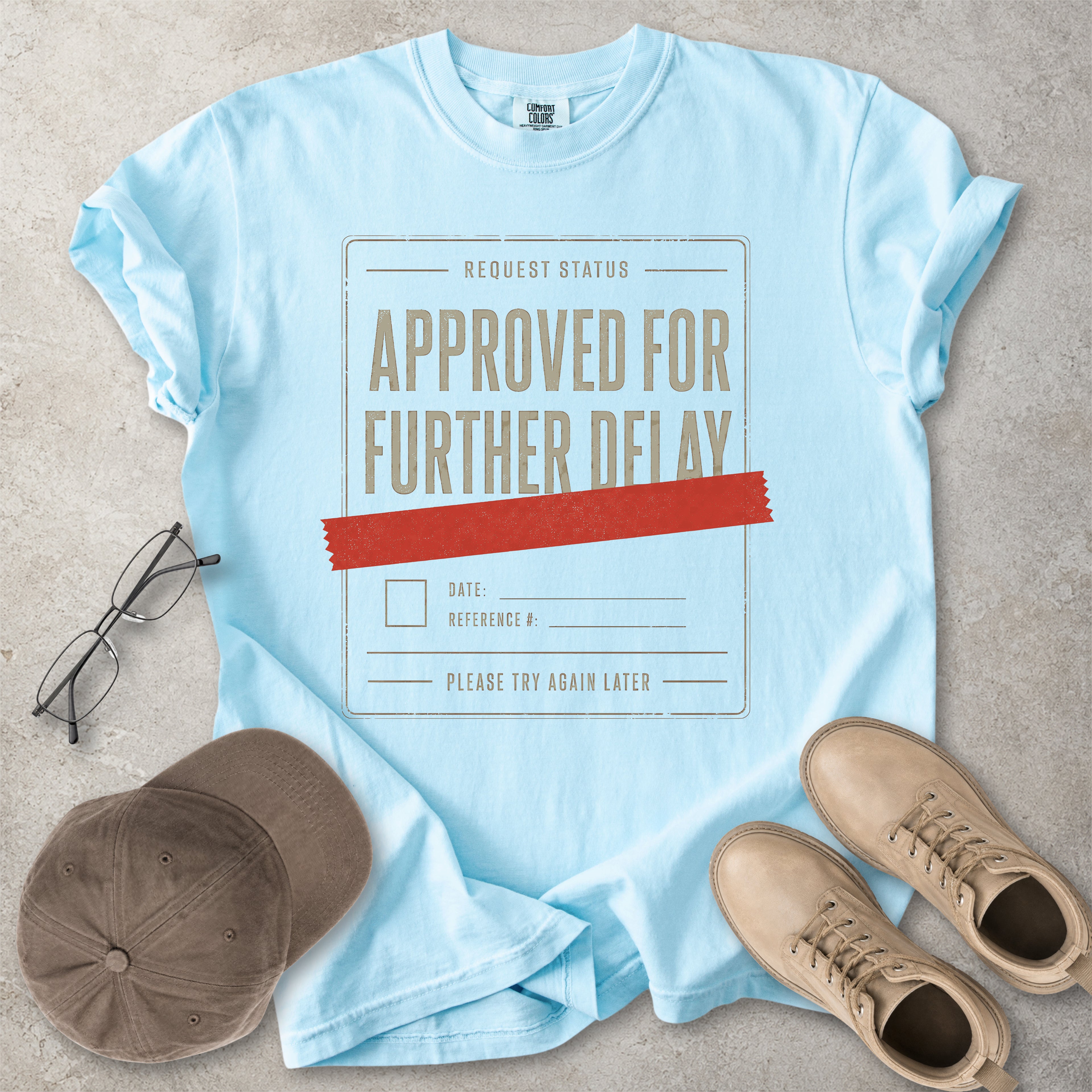 Chambray light blue Comfort Colors 1717 T-shirt with a funny Approved for Further Delay graphic showing a request status form covered with red tape.