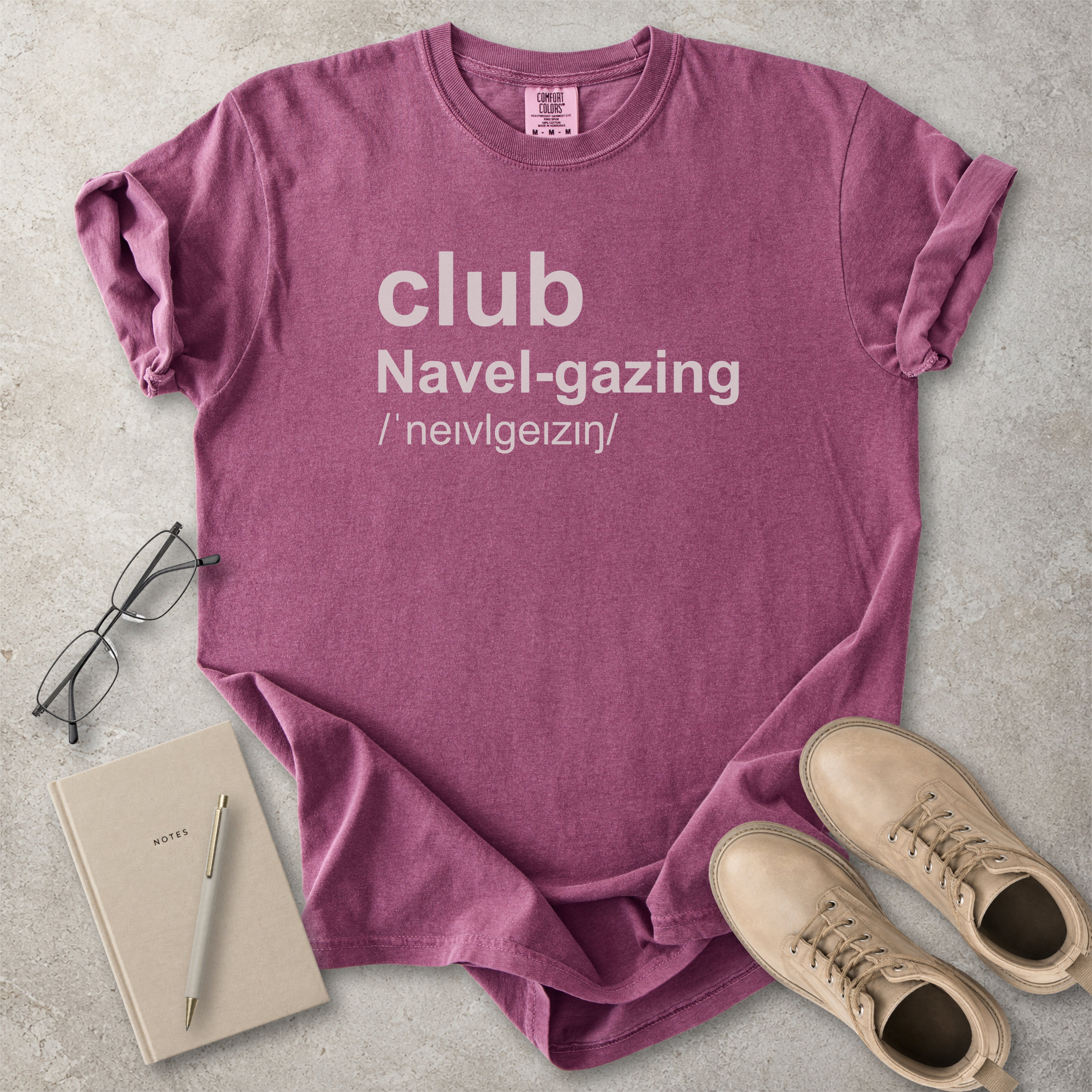 Berry red Comfort Colors graphic T-shirt with grey text reading club navel-gazing, styled with notebook, pen, glasses and tan boots