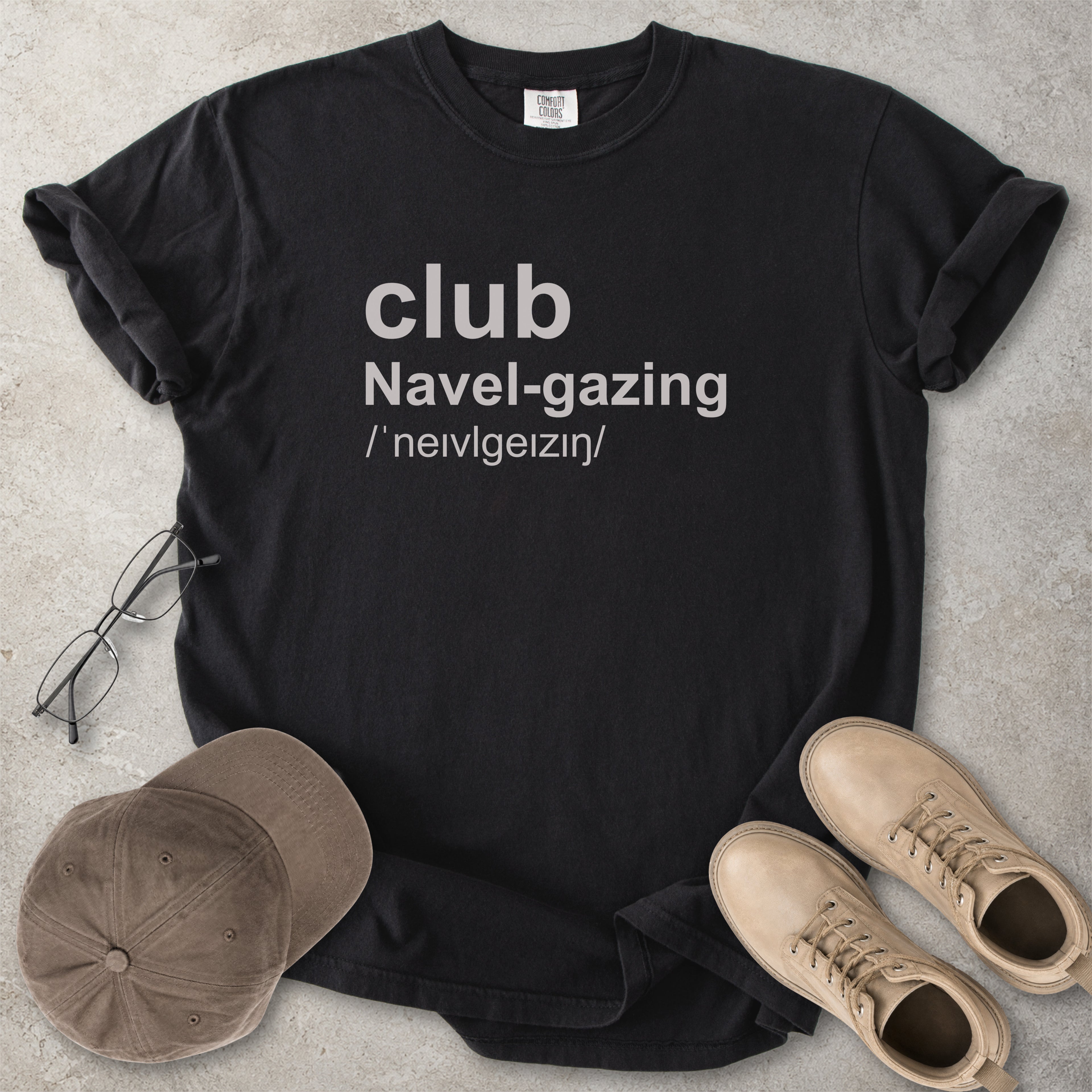 Black Comfort Colors graphic T-shirt with grey text reading club navel-gazing, styled with notebook, pen, glasses and tan boots