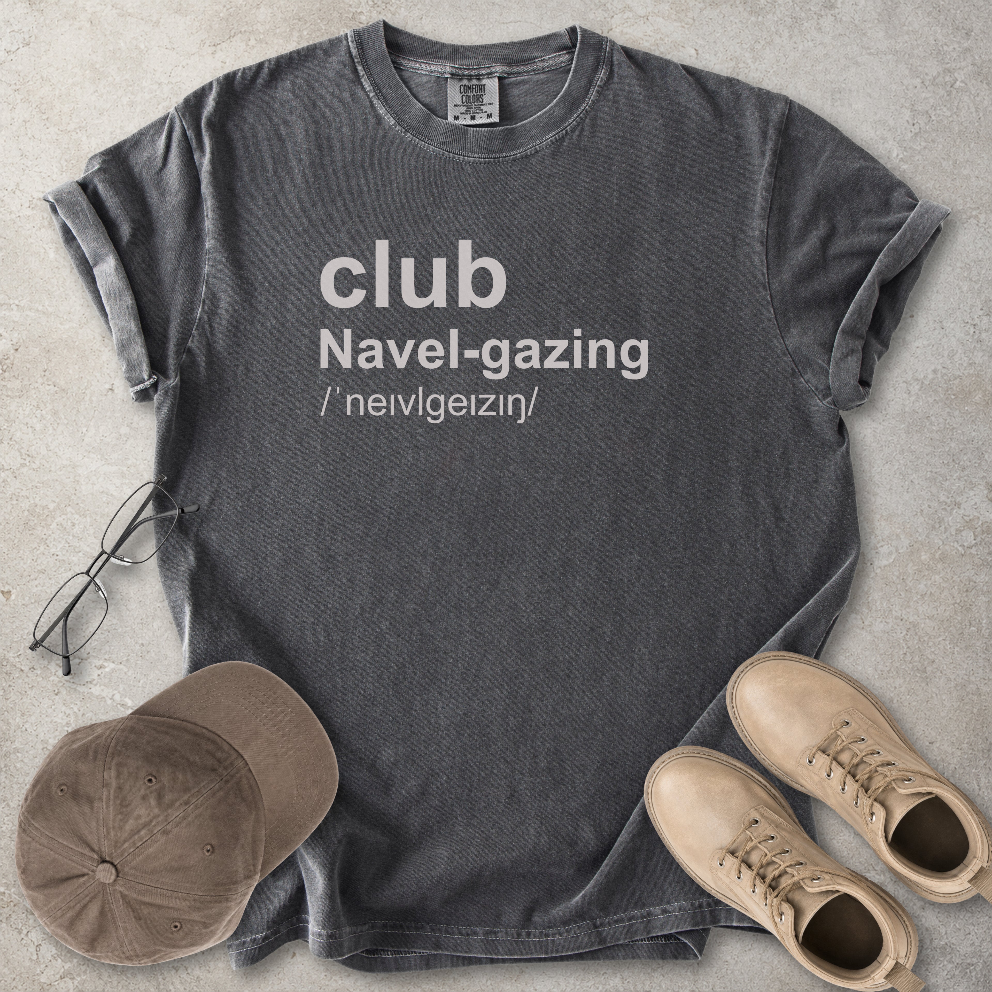 Pepper grey Comfort Colors graphic T-shirt with grey text reading club navel-gazing, styled with notebook, pen, glasses and tan boots