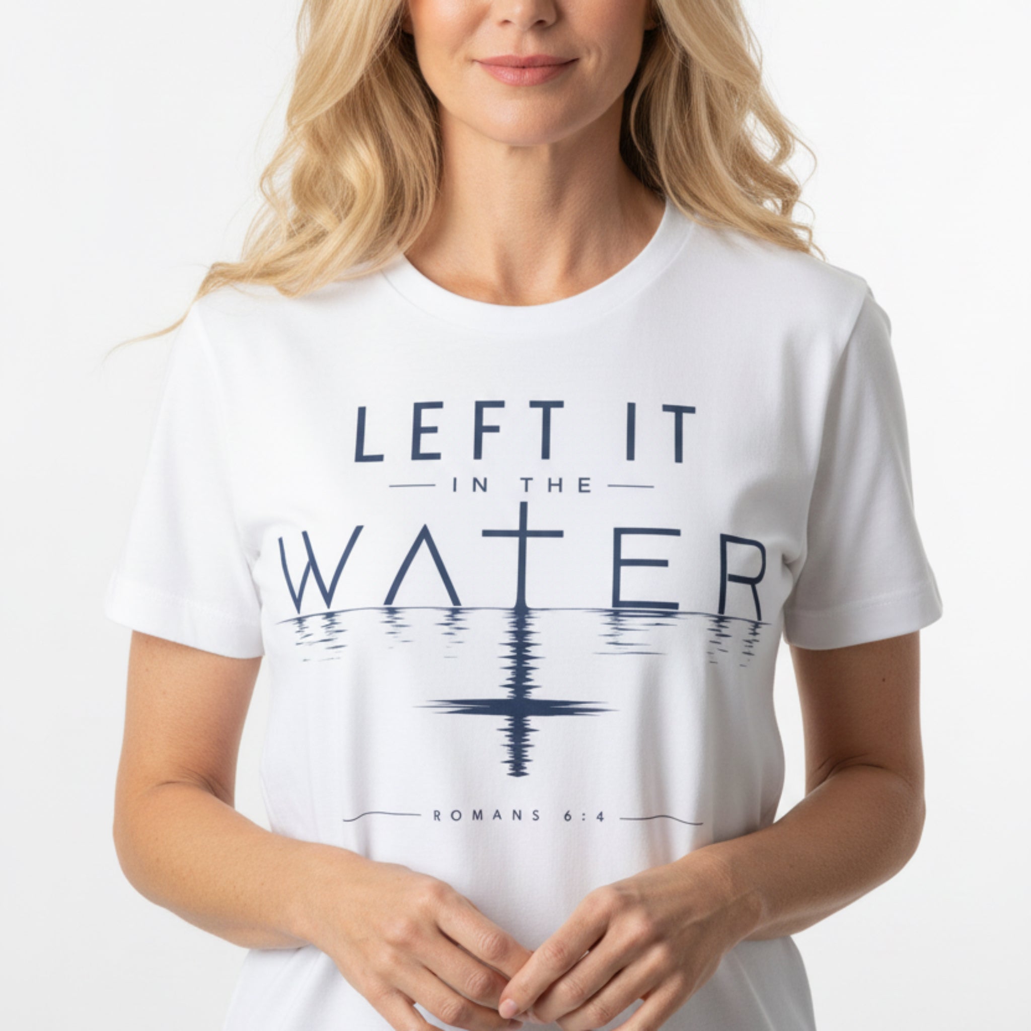 A white short-sleeve crewneck t-shirt with a navy blue graphic print reading 'LEFT IT IN THE WATER' and 'ROMANS 8:4' on a rustic dark wood background.