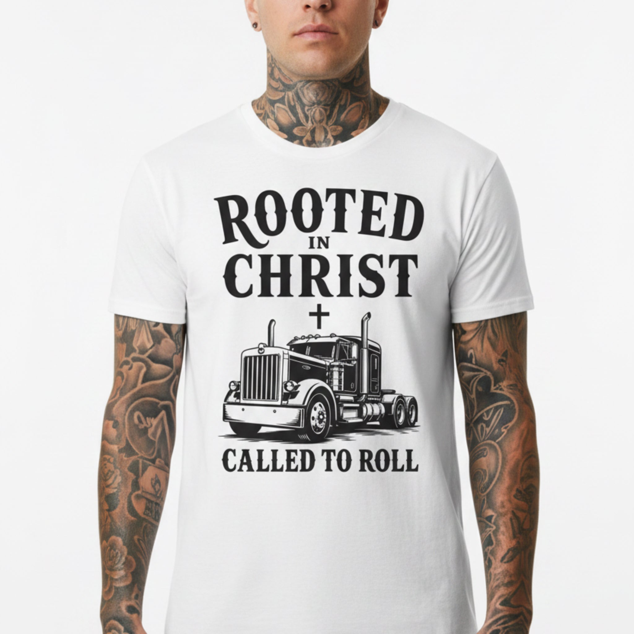 A white short-sleeve graphic T-shirt laid flat on a rustic wooden surface. The shirt features a black printed design with the text 'ROOTED IN CHRIST' above a semi-truck illustration with a cross symbol, and 'CALLED TO ROLL' below.