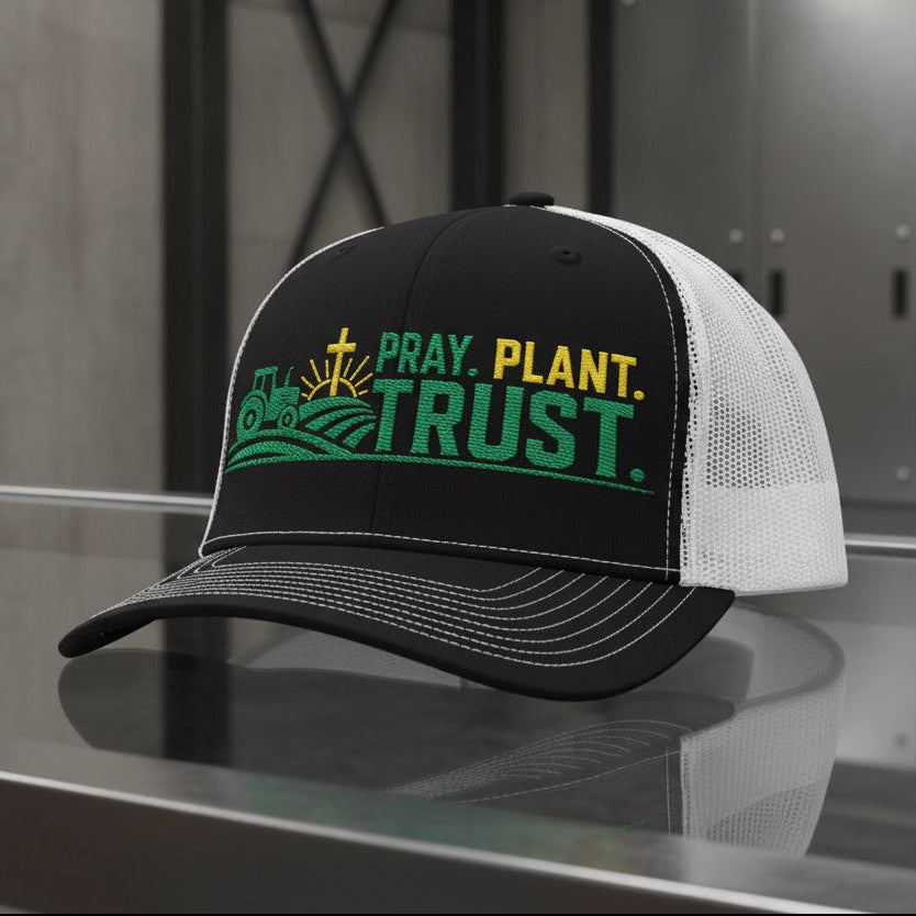 A black and white trucker hat with a green and yellow graphic on the front that reads 'PRAY. PLANT.