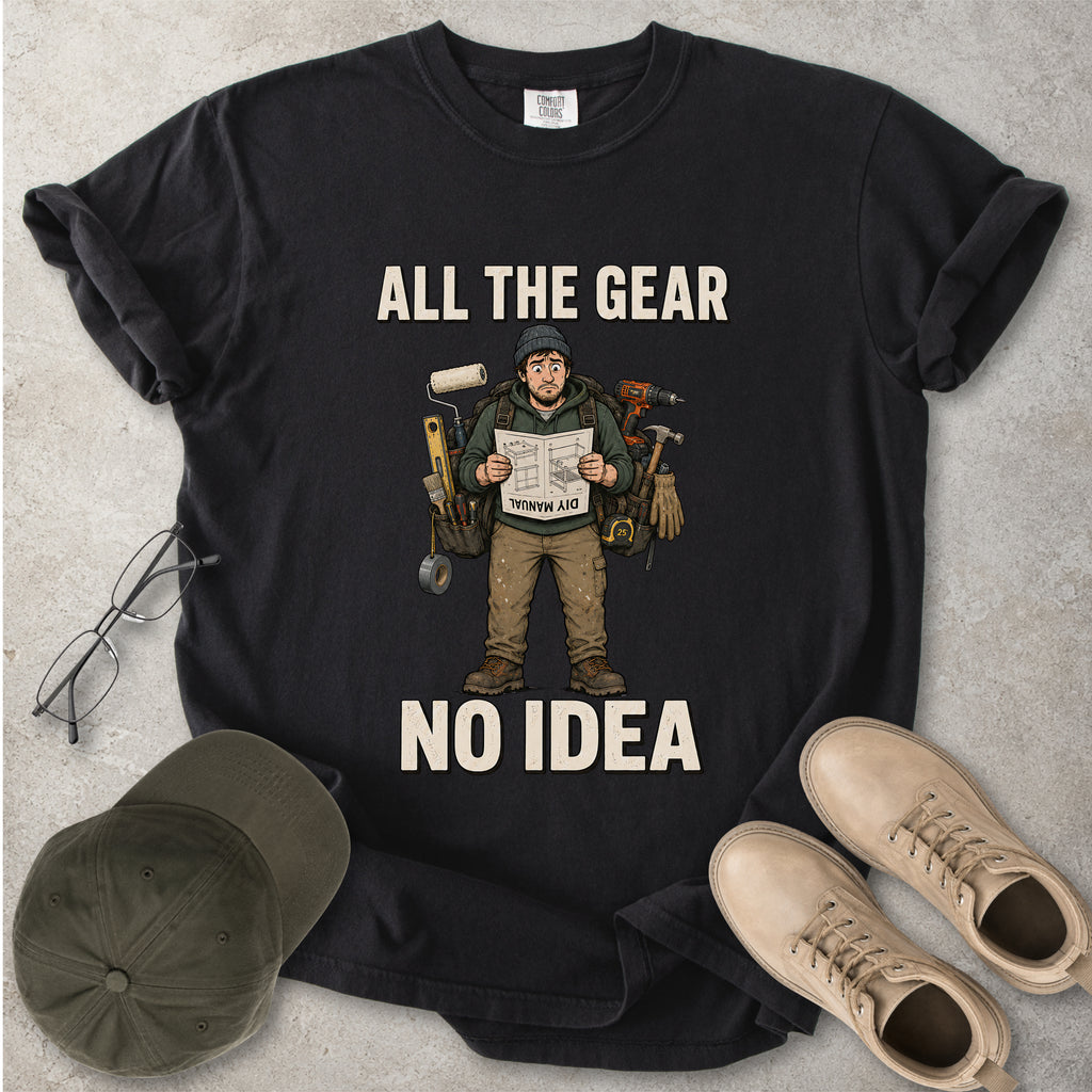 Black t-shirt with graphic design and text 'All the Gear No Idea' on a gray surface with a cap and boots.