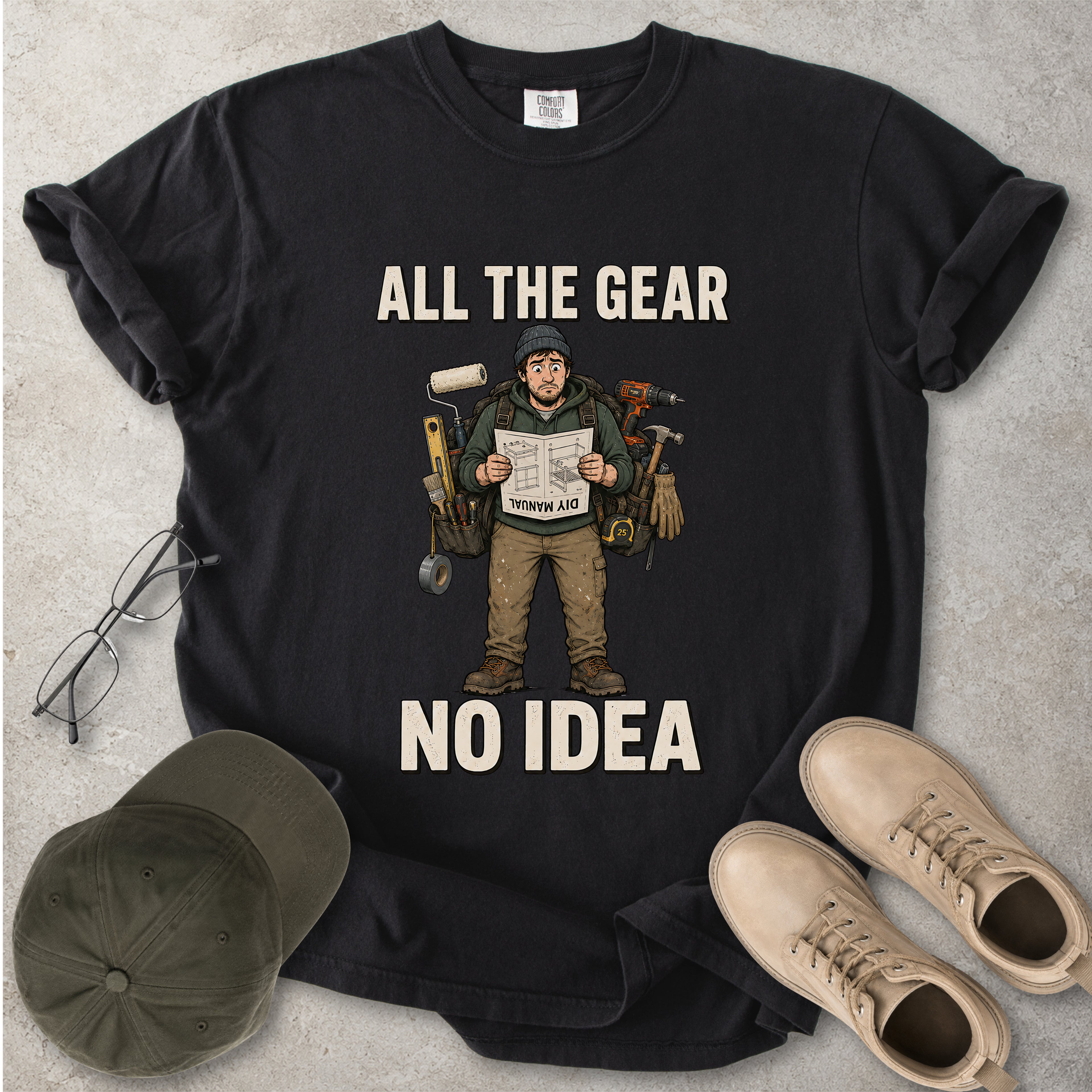 Black t-shirt with graphic design and text 'All the Gear No Idea' on a gray surface with a cap and boots.