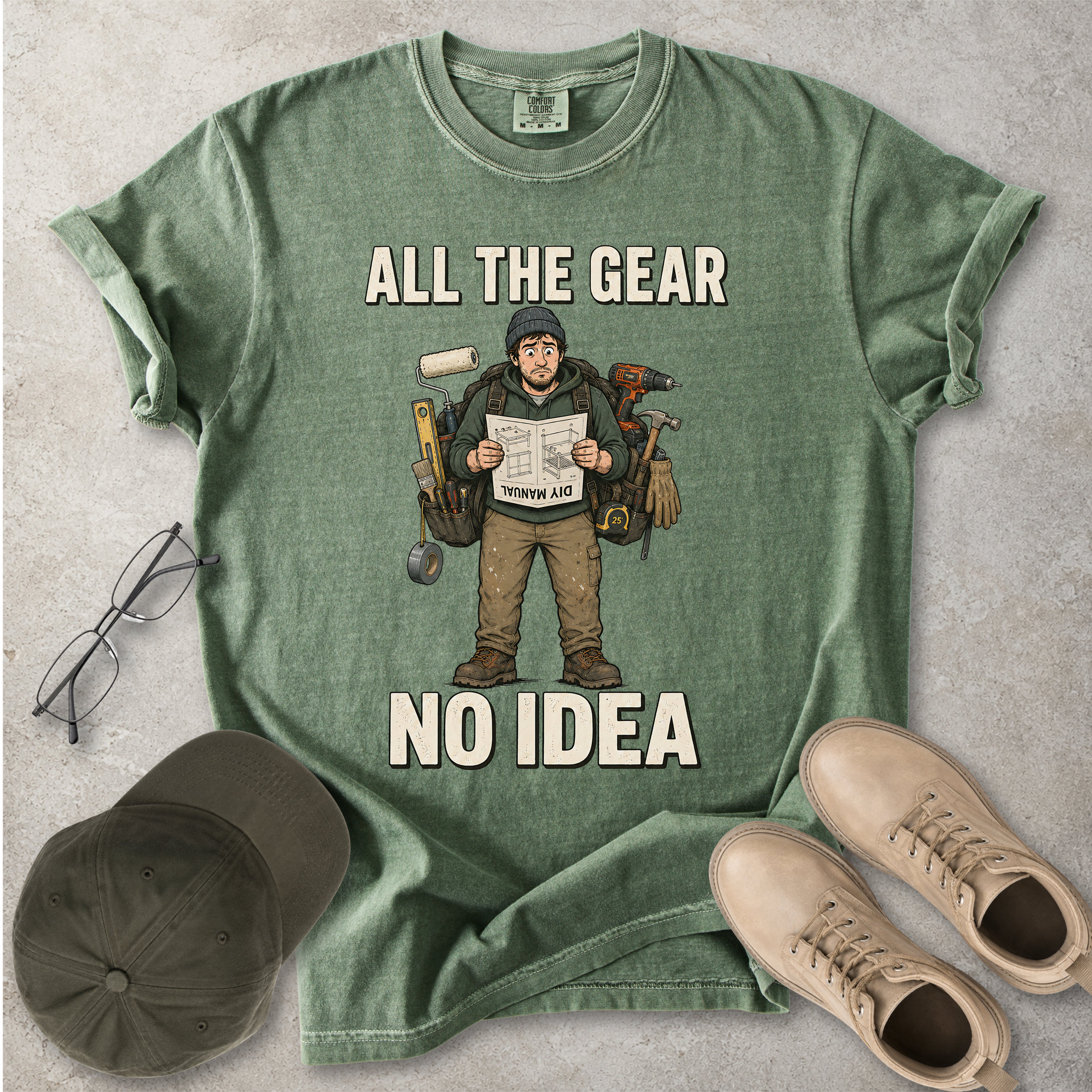 Moss green Comfort Colors 1717 T-shirt with a funny All the Gear No Idea DIY graphic showing a confused handyman carrying tools and reading a manual.