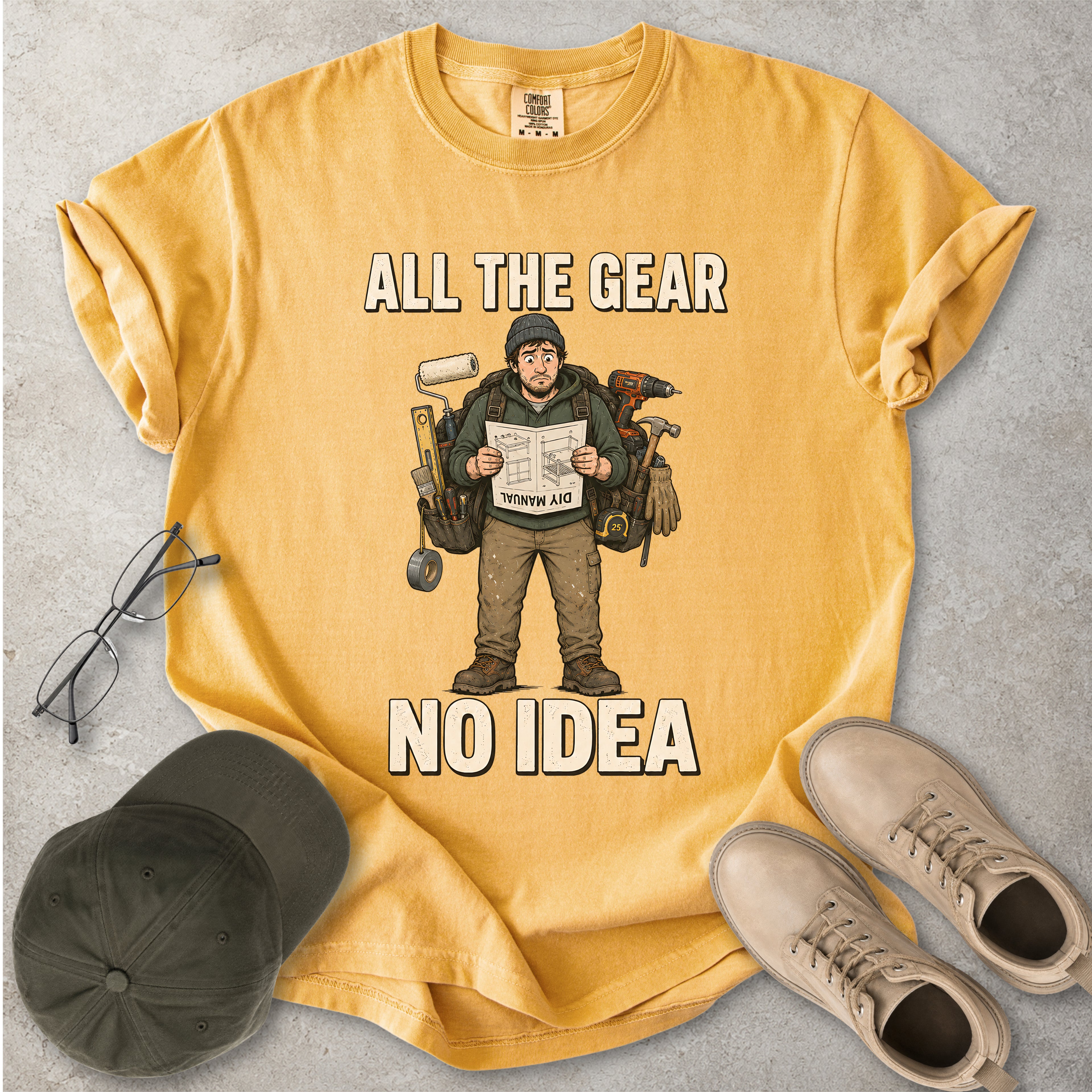 Mustard yellow Comfort Colors 1717 T-shirt with a funny All the Gear No Idea DIY graphic showing a confused handyman carrying tools and reading a manual.
