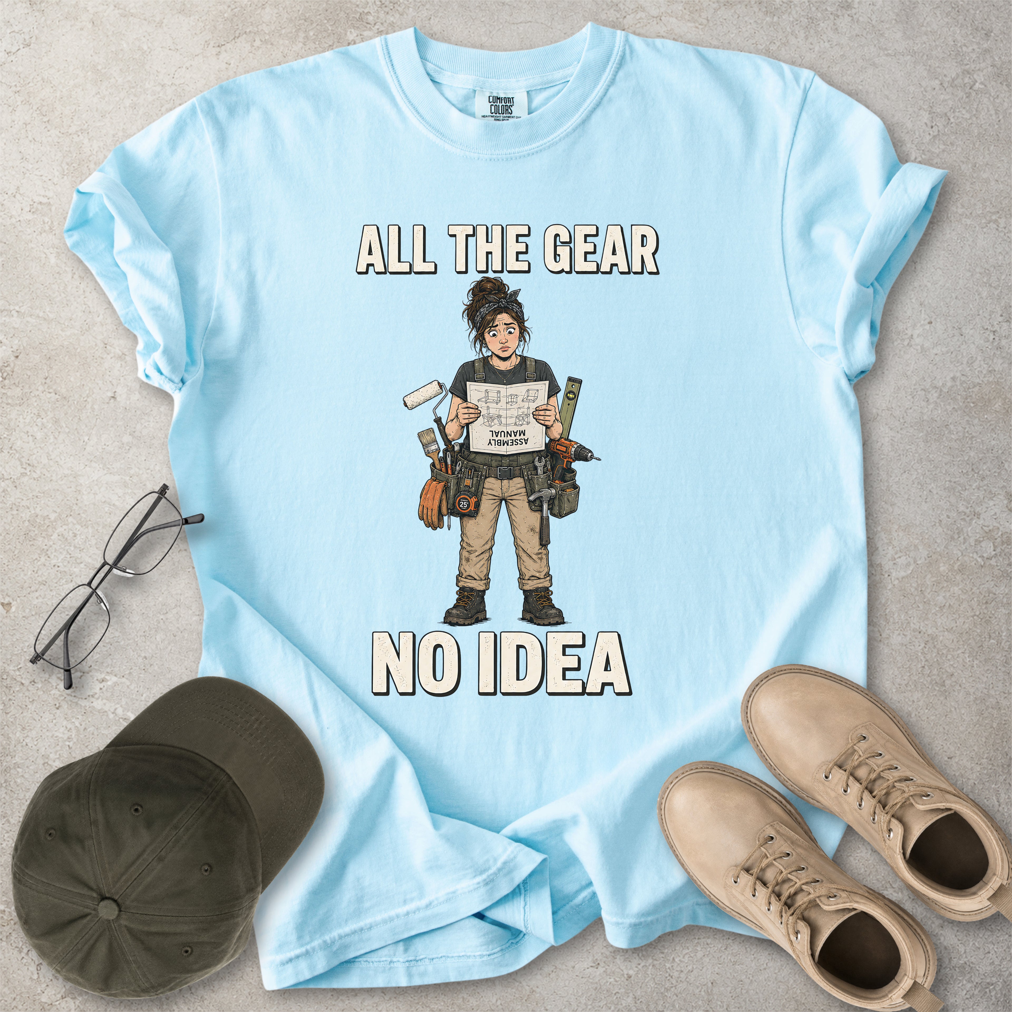 Chambray light blue Comfort Colors 1717 T-shirt with a funny All the Gear No Idea DIY graphic showing a woman with tools holding an upside-down assembly manual.