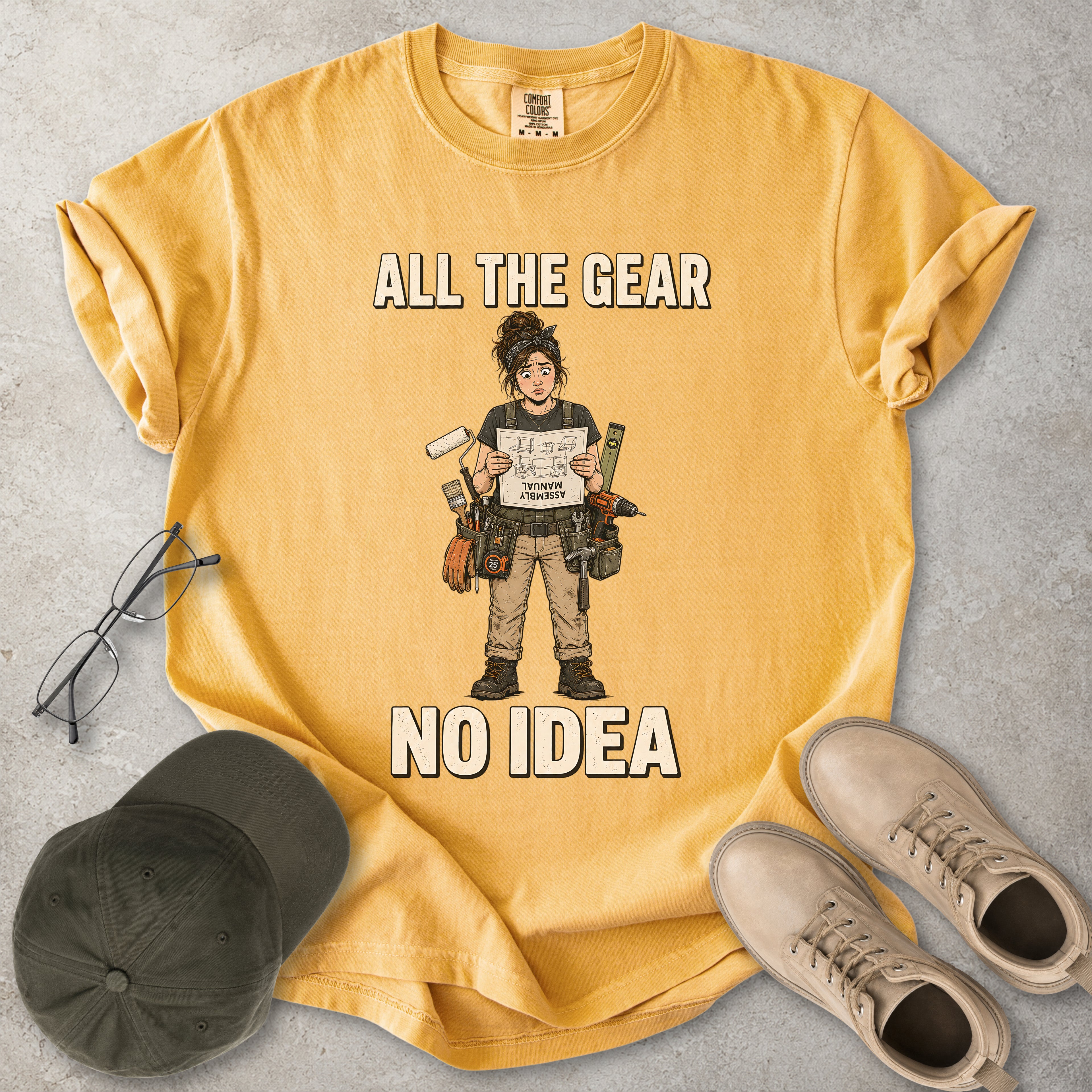 Mustard yellow Comfort Colors 1717 T-shirt with a funny All the Gear No Idea DIY graphic showing a woman with tools holding an upside-down assembly manual.