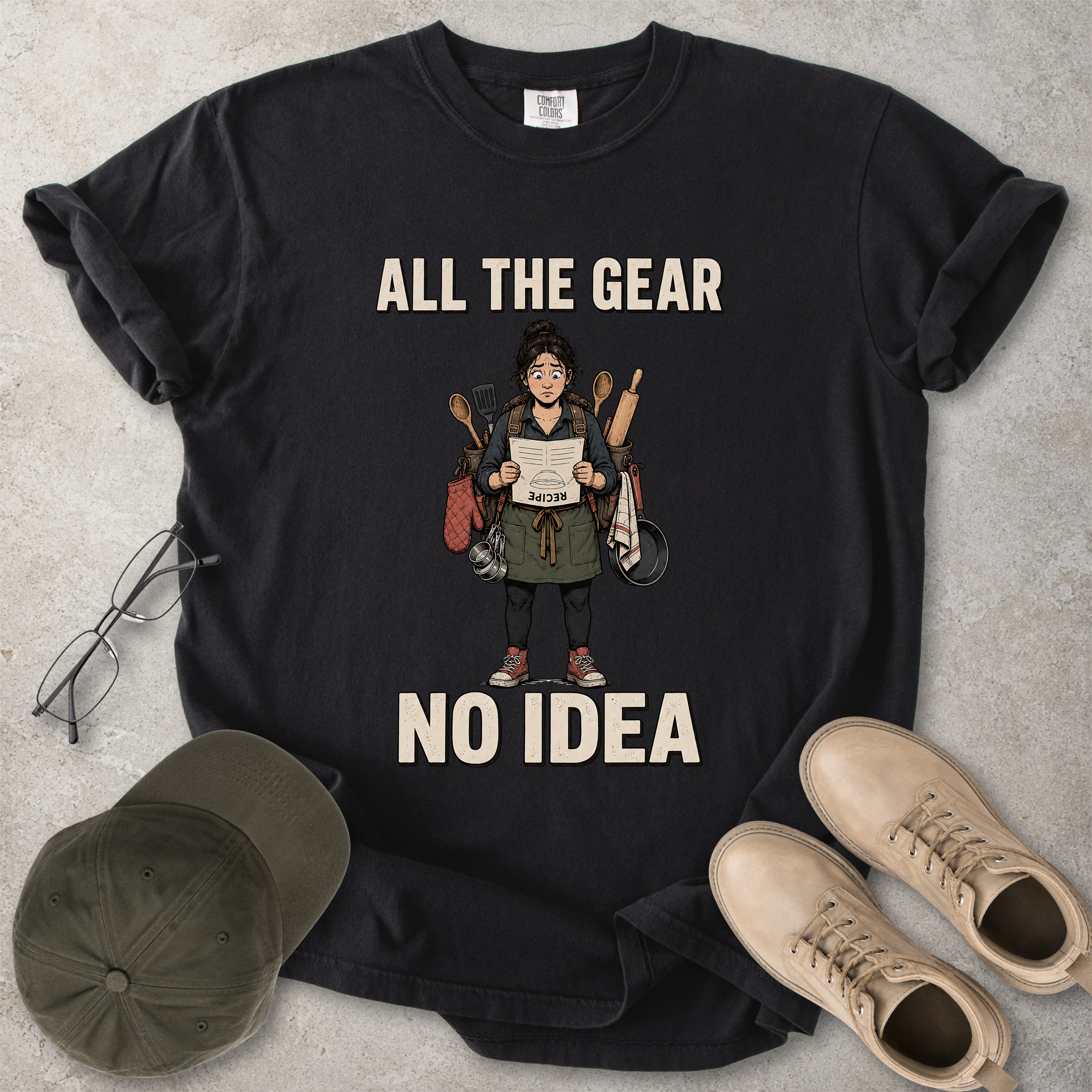 Black Comfort Colors 1717 T-shirt with a funny All the Gear No Idea cooking graphic showing a woman holding an upside-down recipe with kitchen utensils.