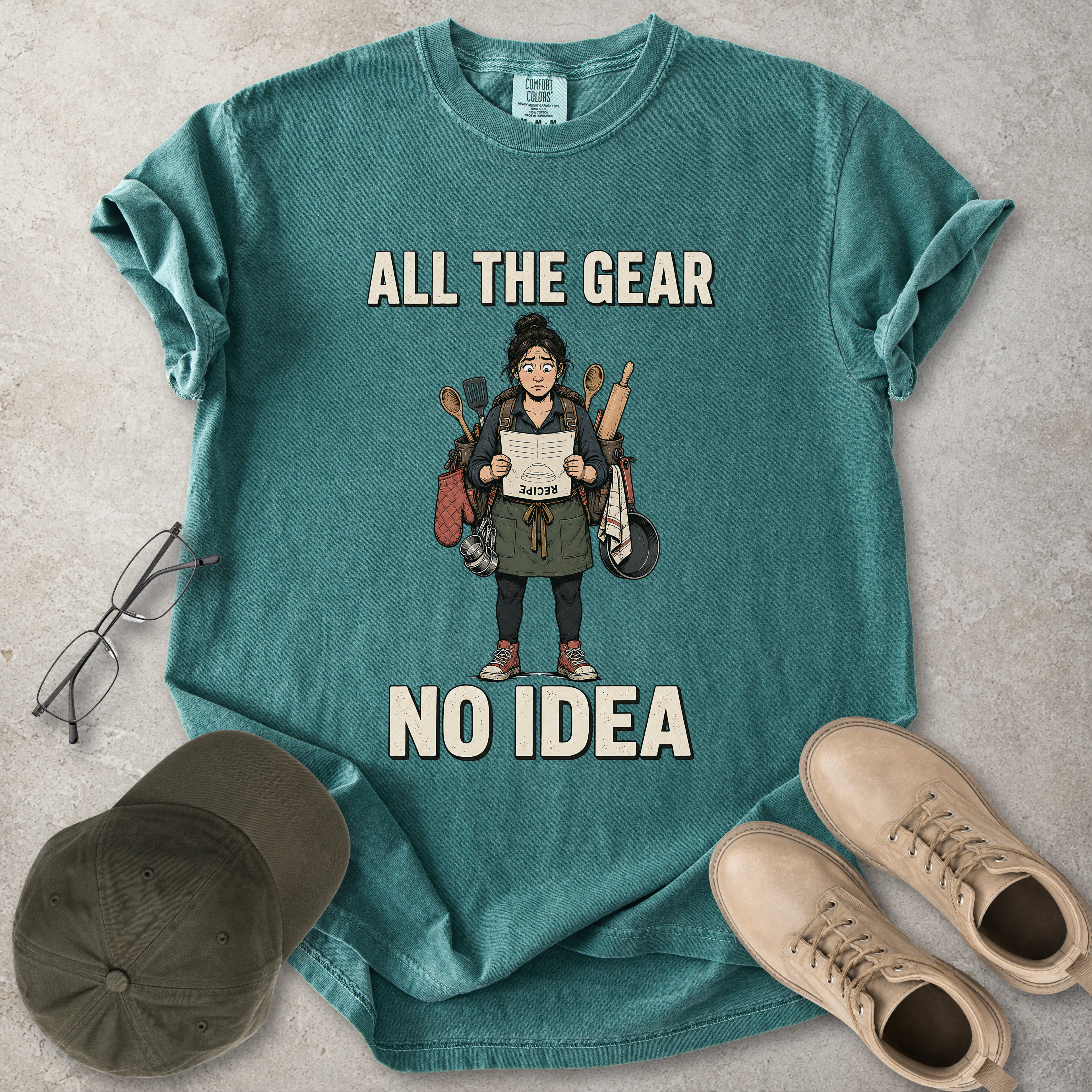 Blue spruce Comfort Colors 1717 T-shirt with a funny All the Gear No Idea cooking graphic showing a woman holding an upside-down recipe with kitchen utensils.