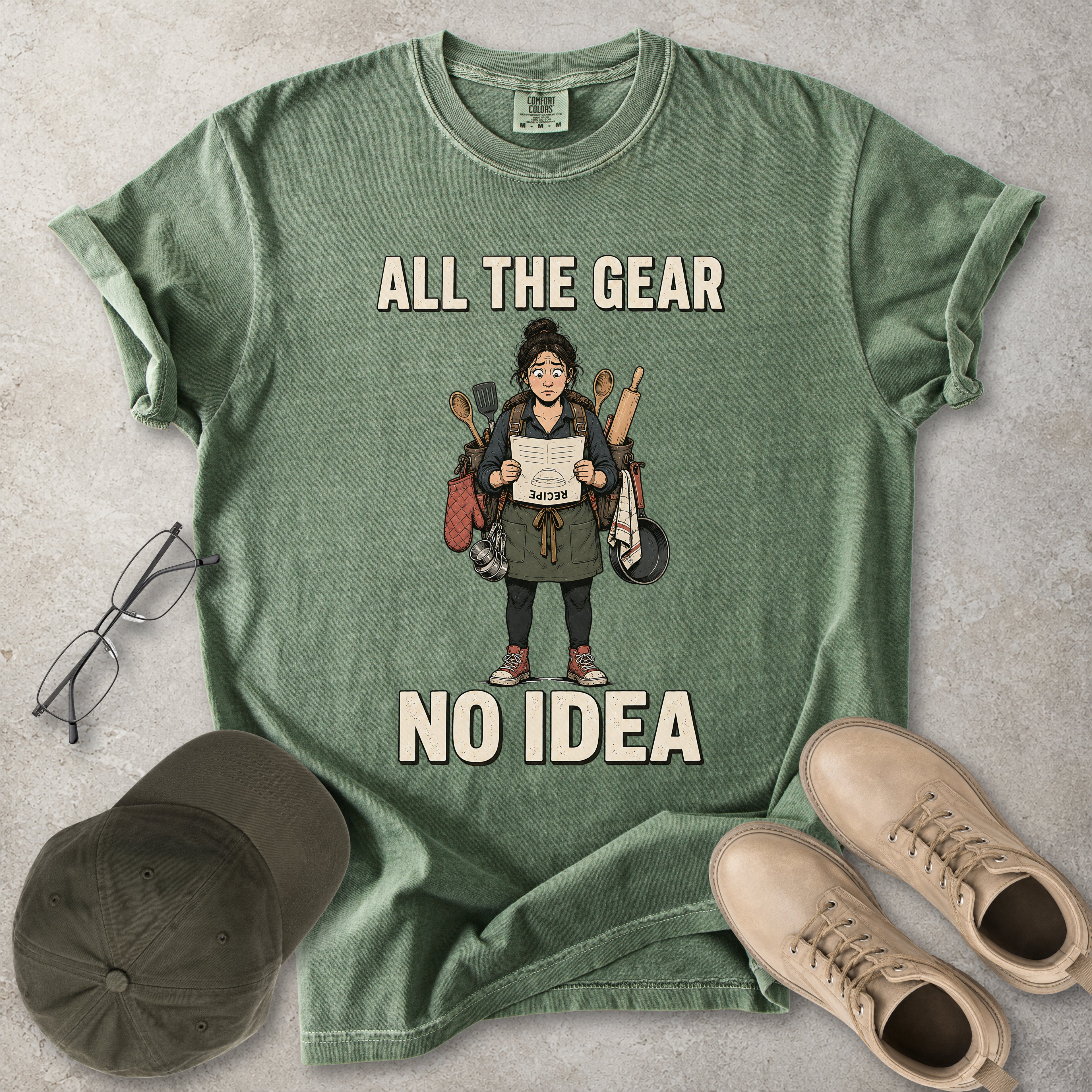 Moss green Comfort Colors 1717 T-shirt with a funny All the Gear No Idea cooking graphic showing a woman holding an upside-down recipe with kitchen utensils.