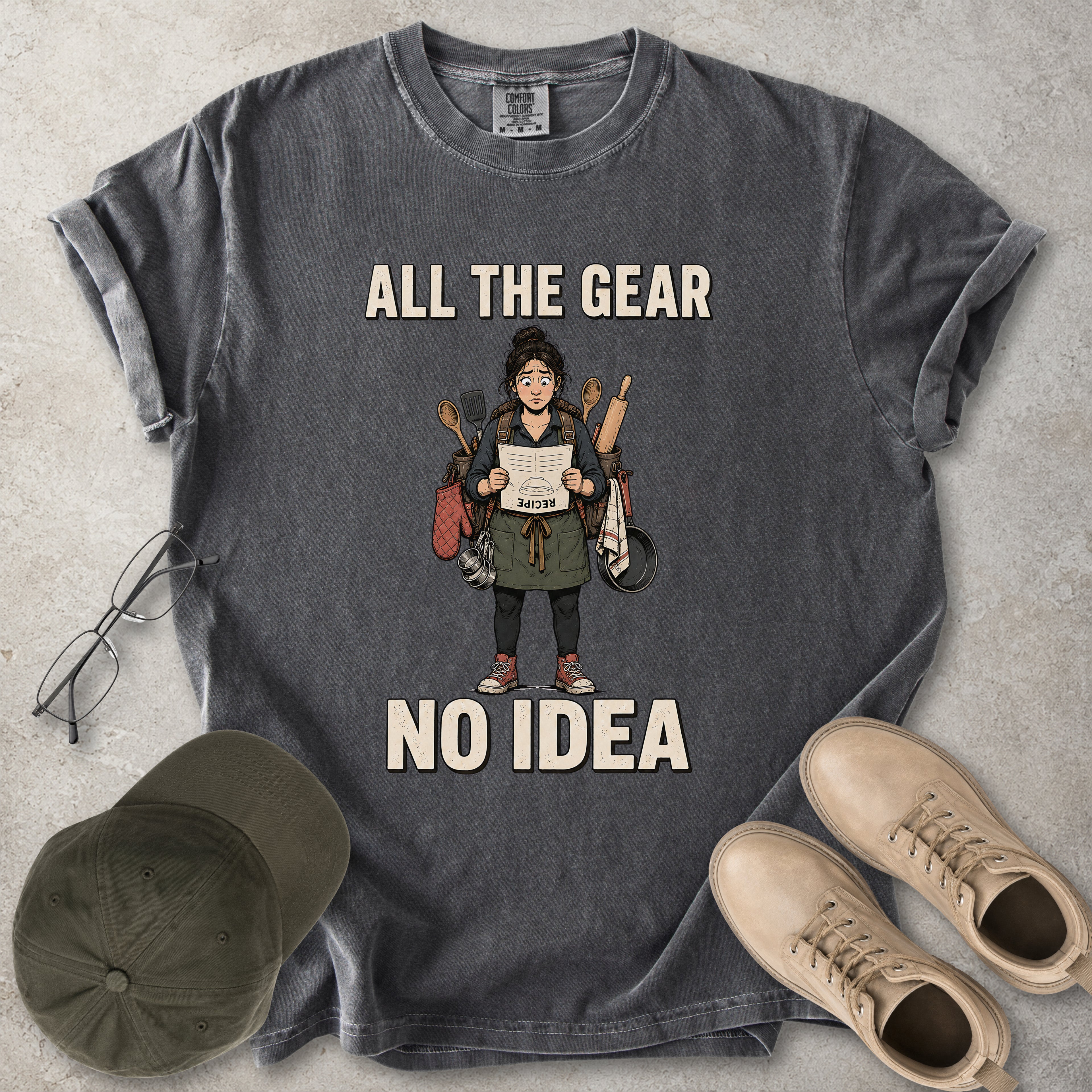Pepper grey Comfort Colors 1717 T-shirt with a funny All the Gear No Idea cooking graphic showing a woman holding an upside-down recipe with kitchen utensils.