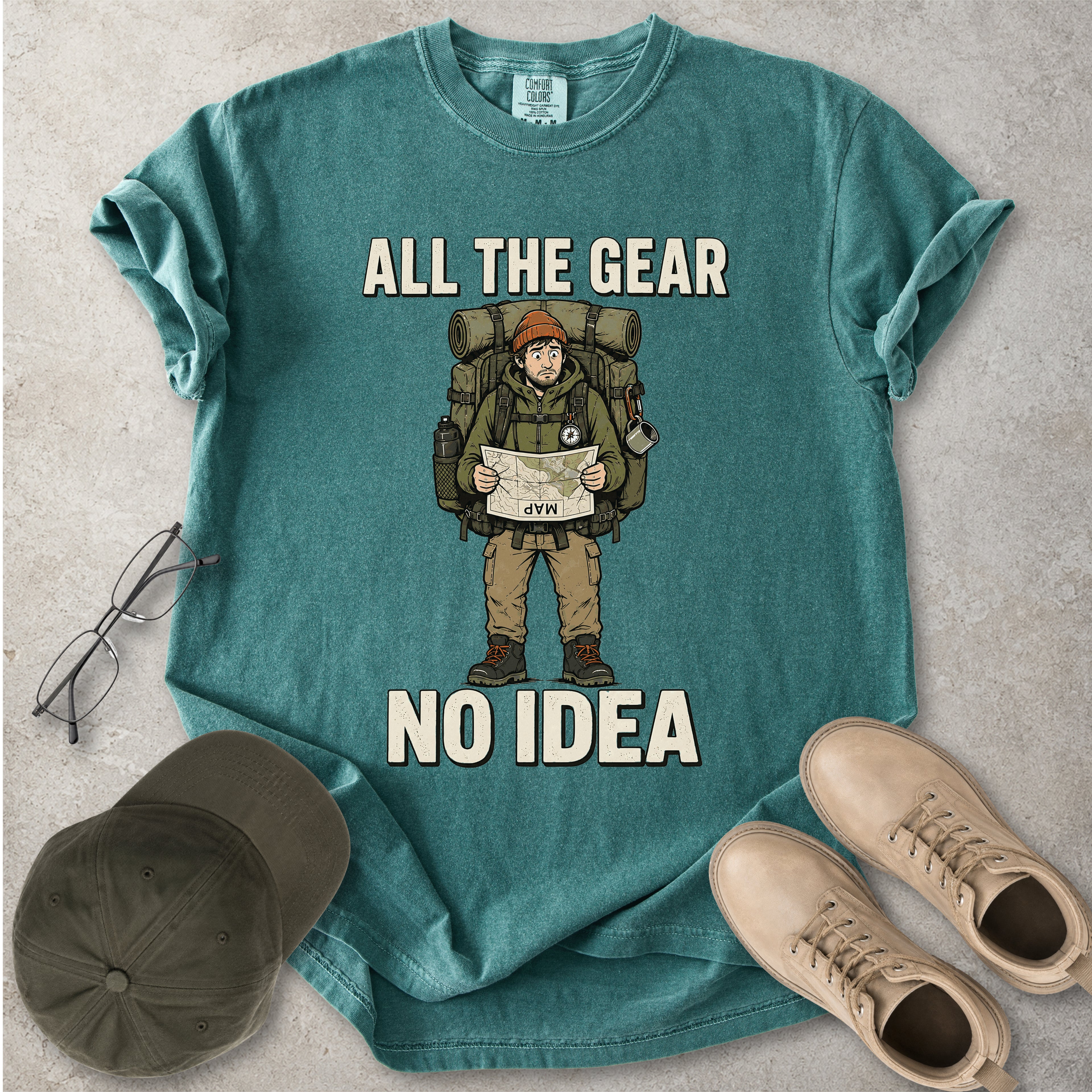 Blue spruce Comfort Colors 1717 T-shirt with a funny All the Gear No Idea hiking graphic showing a confused hiker holding an upside-down map with a large backpack.