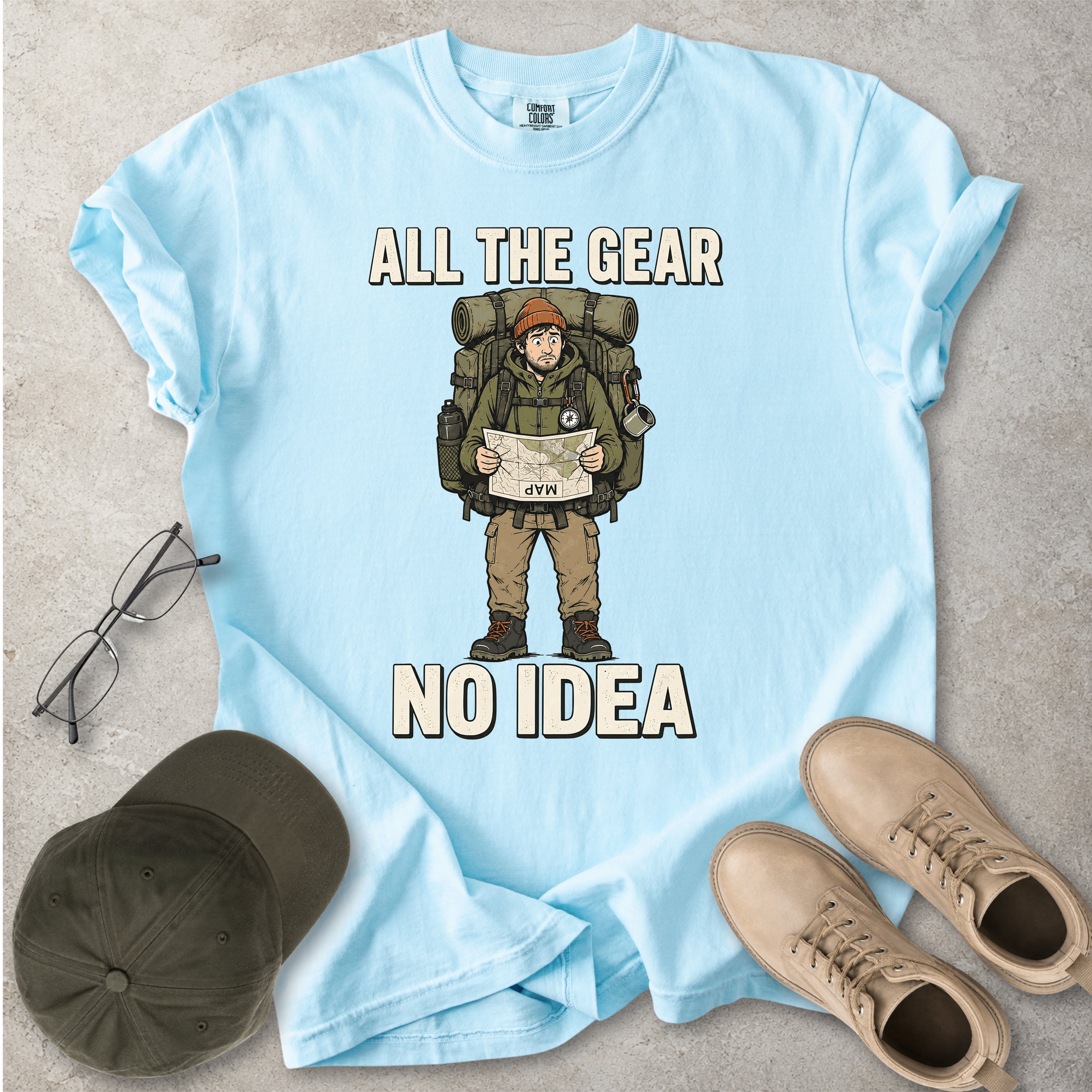 Chambray light blue Comfort Colors 1717 T-shirt with a funny All the Gear No Idea hiking graphic showing a confused hiker holding an upside-down map with a large backpack.