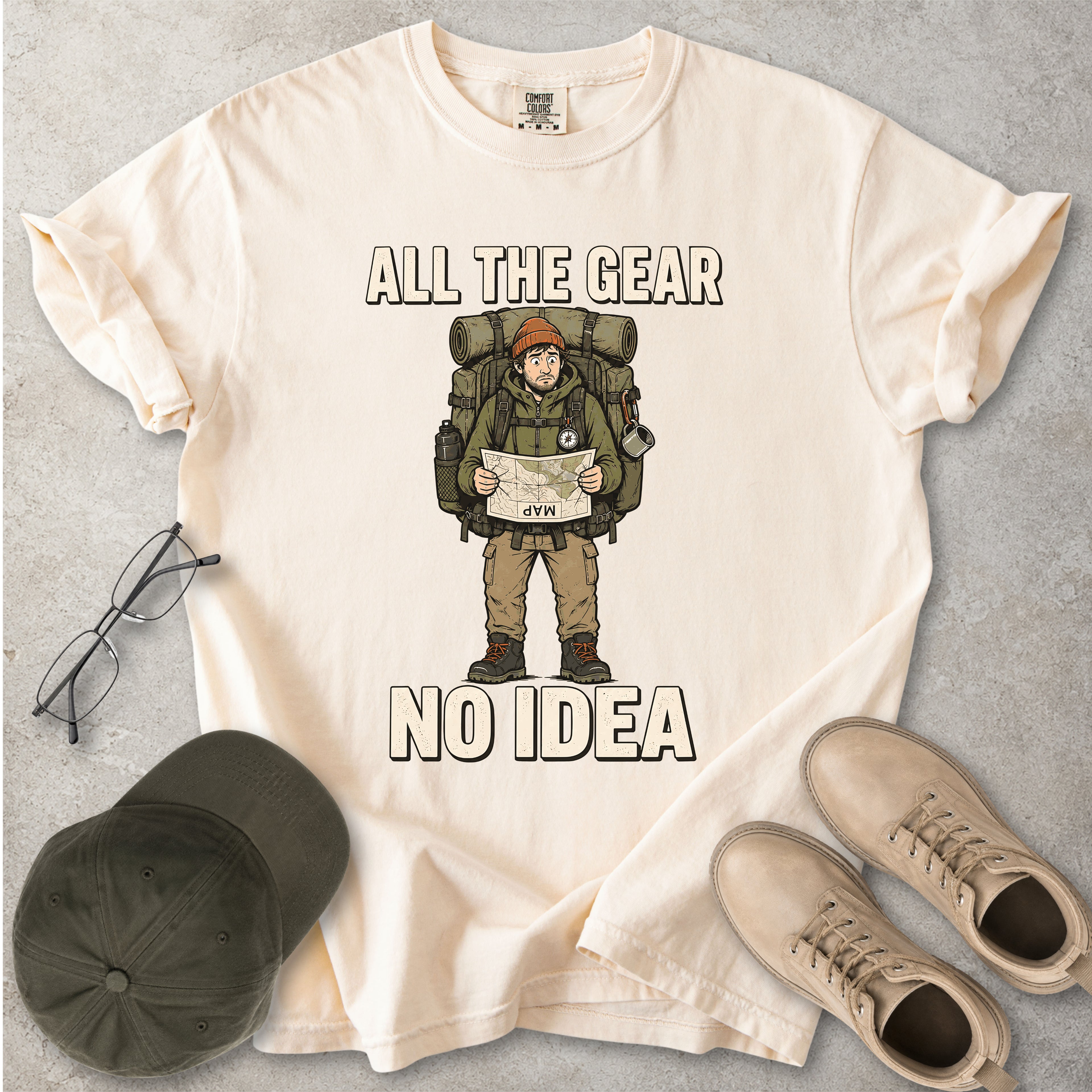 Ivory beige Comfort Colors 1717 T-shirt with a funny All the Gear No Idea hiking graphic showing a confused hiker holding an upside-down map with a large backpack.