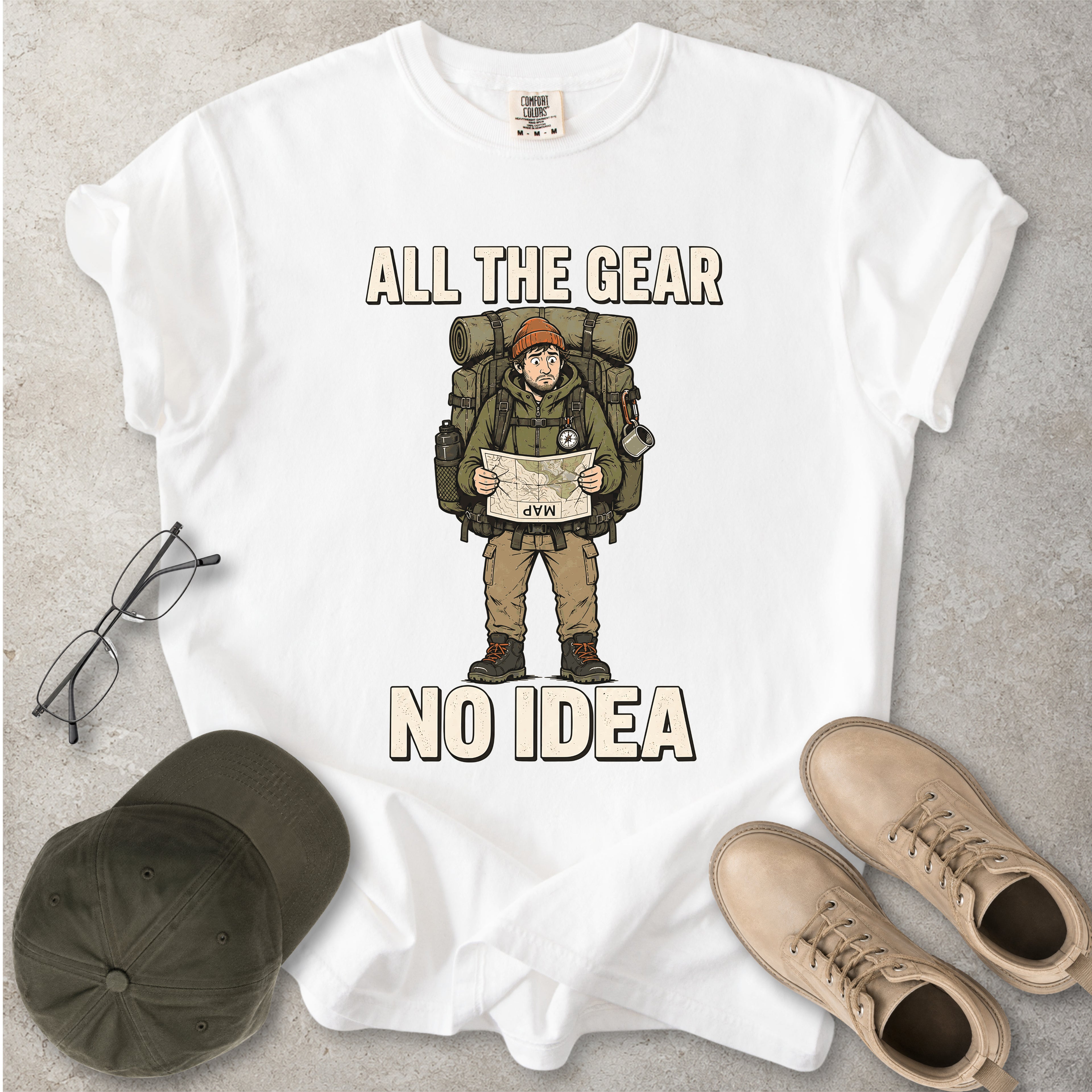 White Comfort Colors 1717 T-shirt with a funny All the Gear No Idea hiking graphic showing a confused hiker holding an upside-down map with a large backpack.