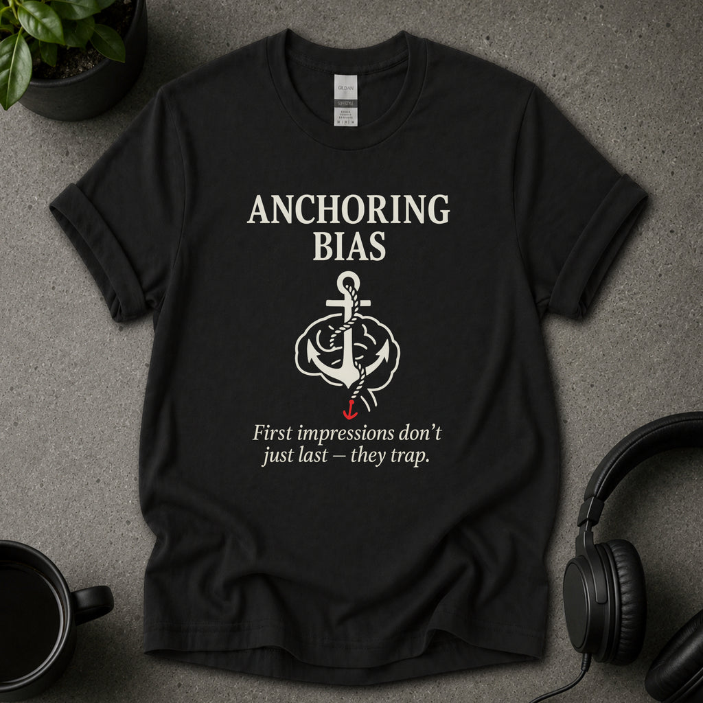 Black t-shirt with 'Anchoring Bias' graphic and text on a gray surface with a plant and headphones.