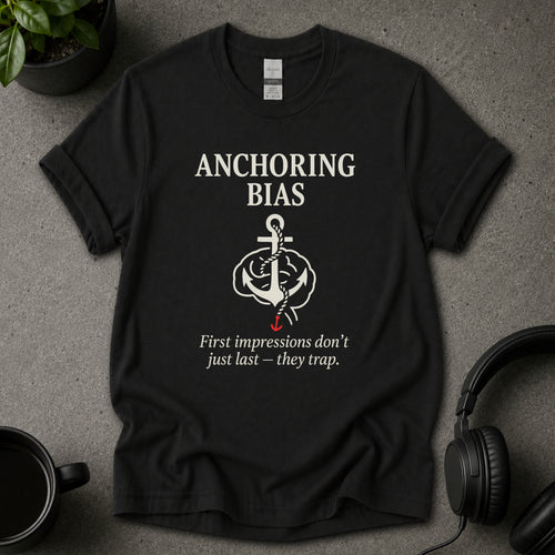 Black t-shirt with 'Anchoring Bias' graphic and text on a gray surface with a plant and headphones.