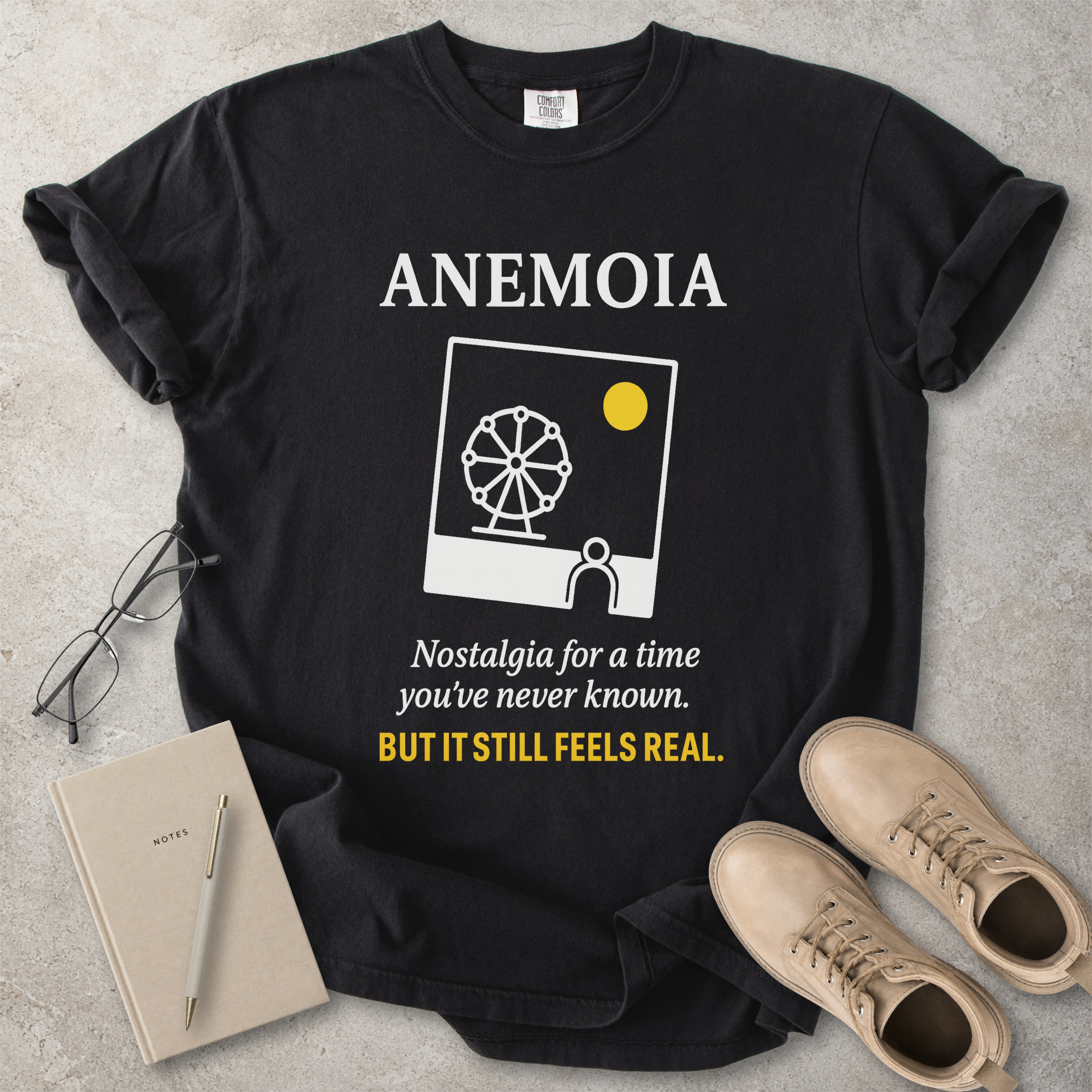 Black t-shirt with 'Anemoia' design and text on a concrete surface with accessories.