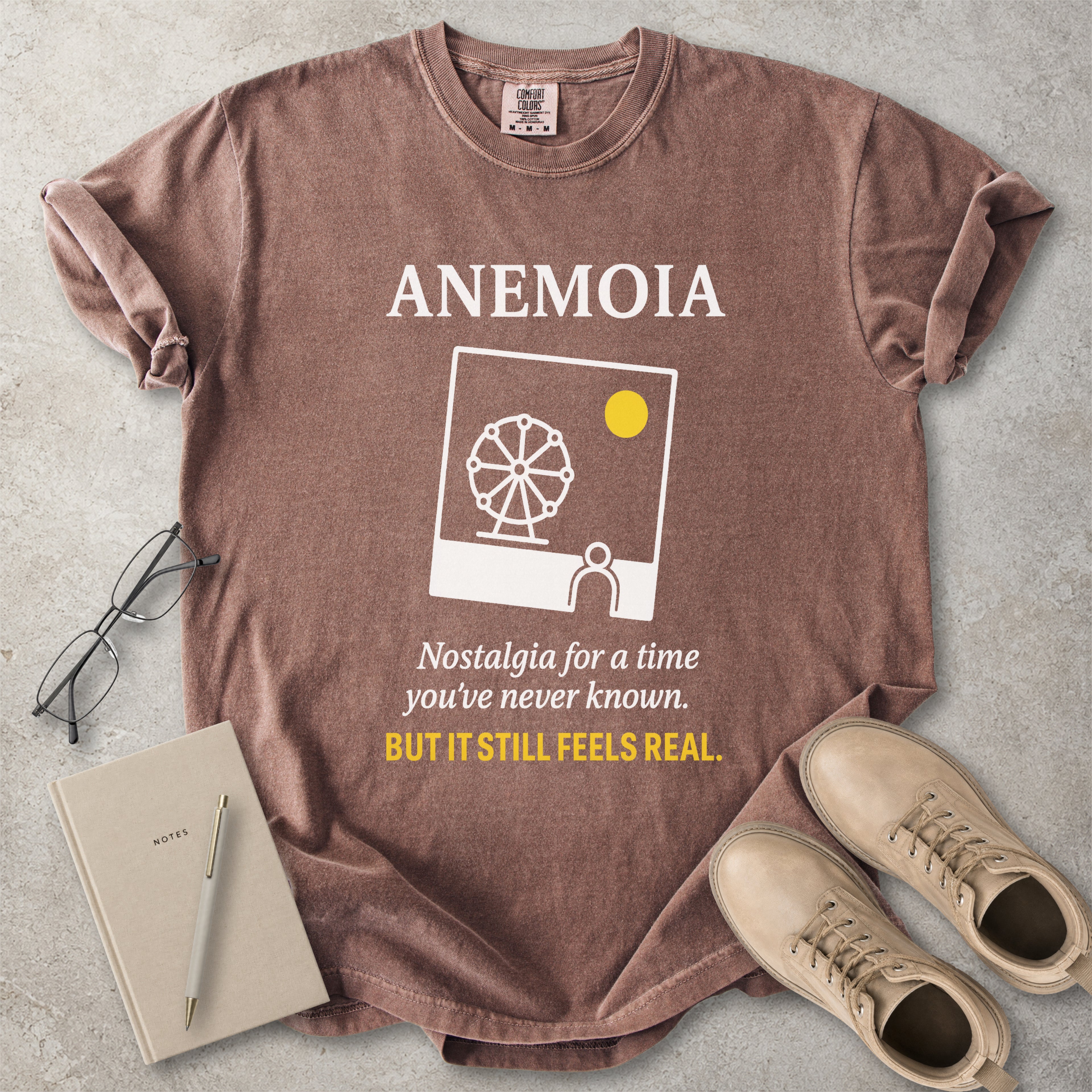 Espresso brown Comfort Colors graphic T-shirt with Anemoia text, photo-style ferris wheel design and yellow accent text, styled with notebook, glasses and tan boots