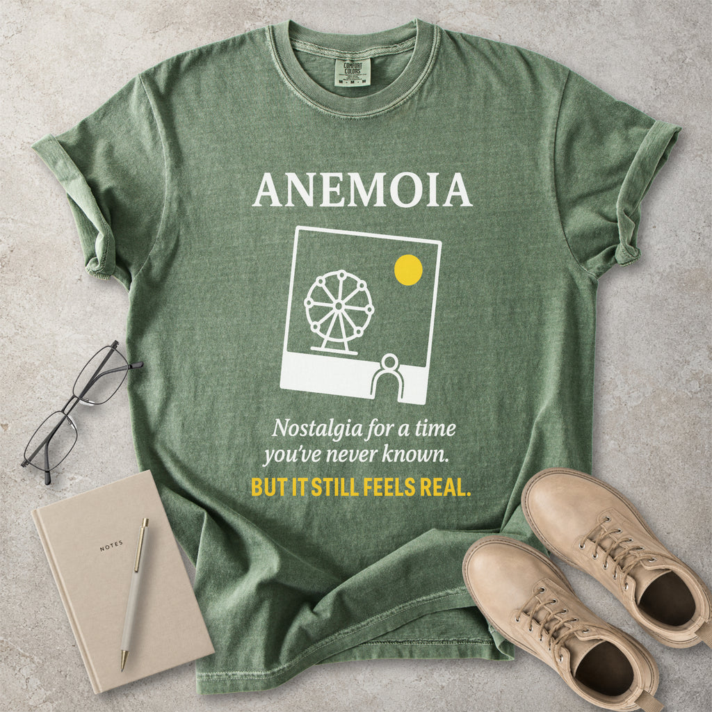 Green t-shirt with 'Anemoia' design and text on a concrete surface with shoes and notebook.