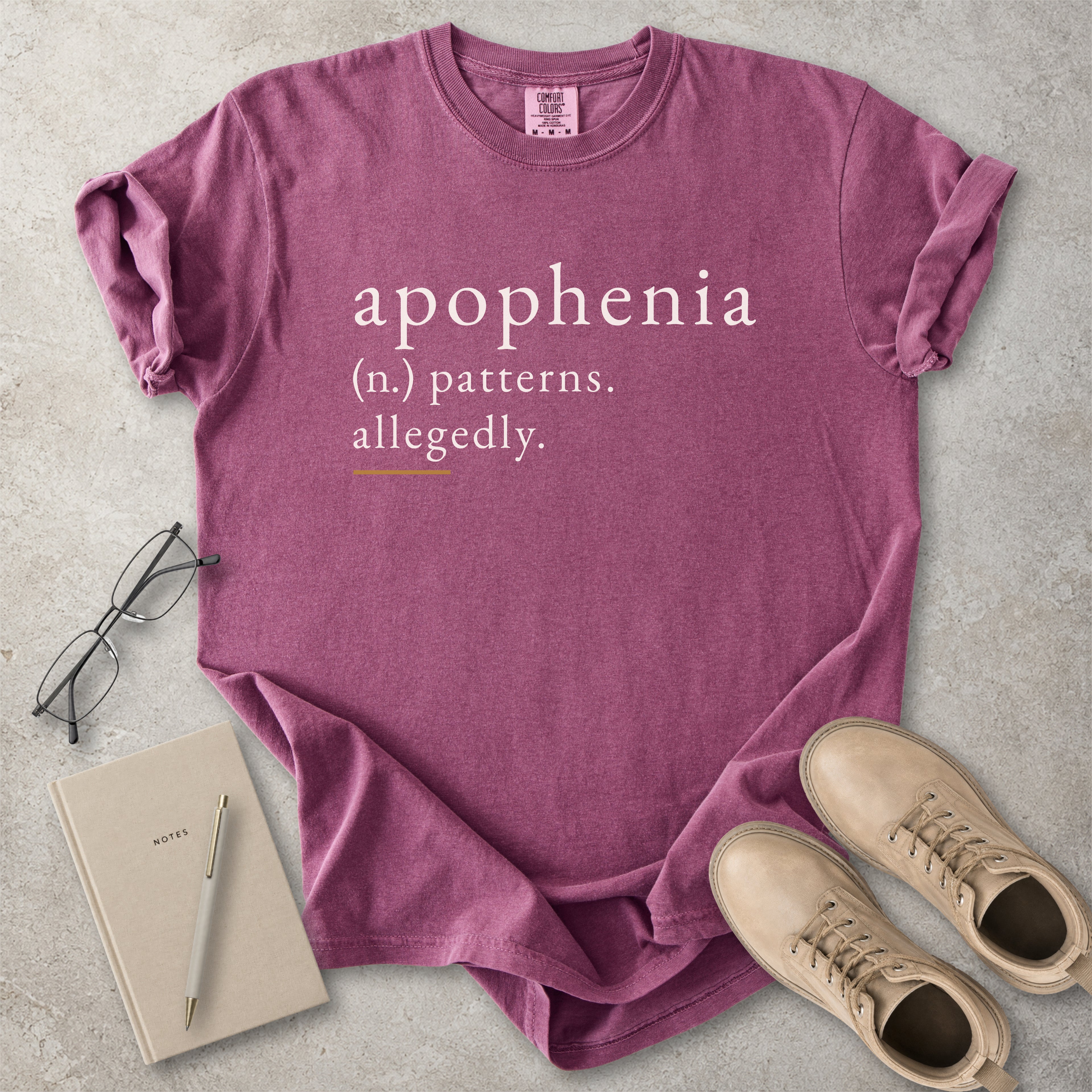 Berry red Comfort Colors graphic T-shirt with apophenia definition text reading patterns allegedly, styled with notebook, pen, glasses and tan boots