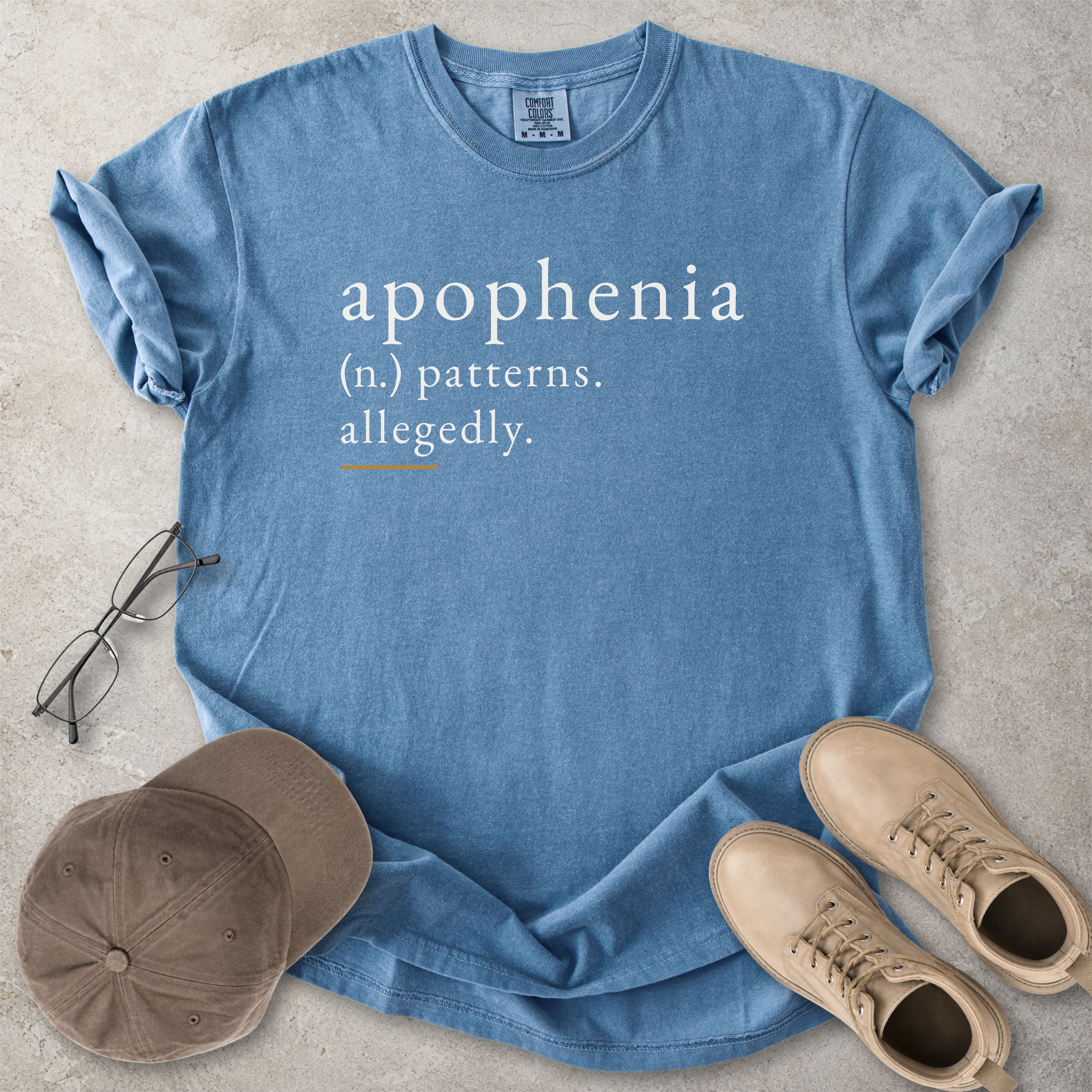 Blue jean Comfort Colors graphic T-shirt with apophenia definition text reading patterns allegedly, styled with notebook, pen, glasses and tan boots