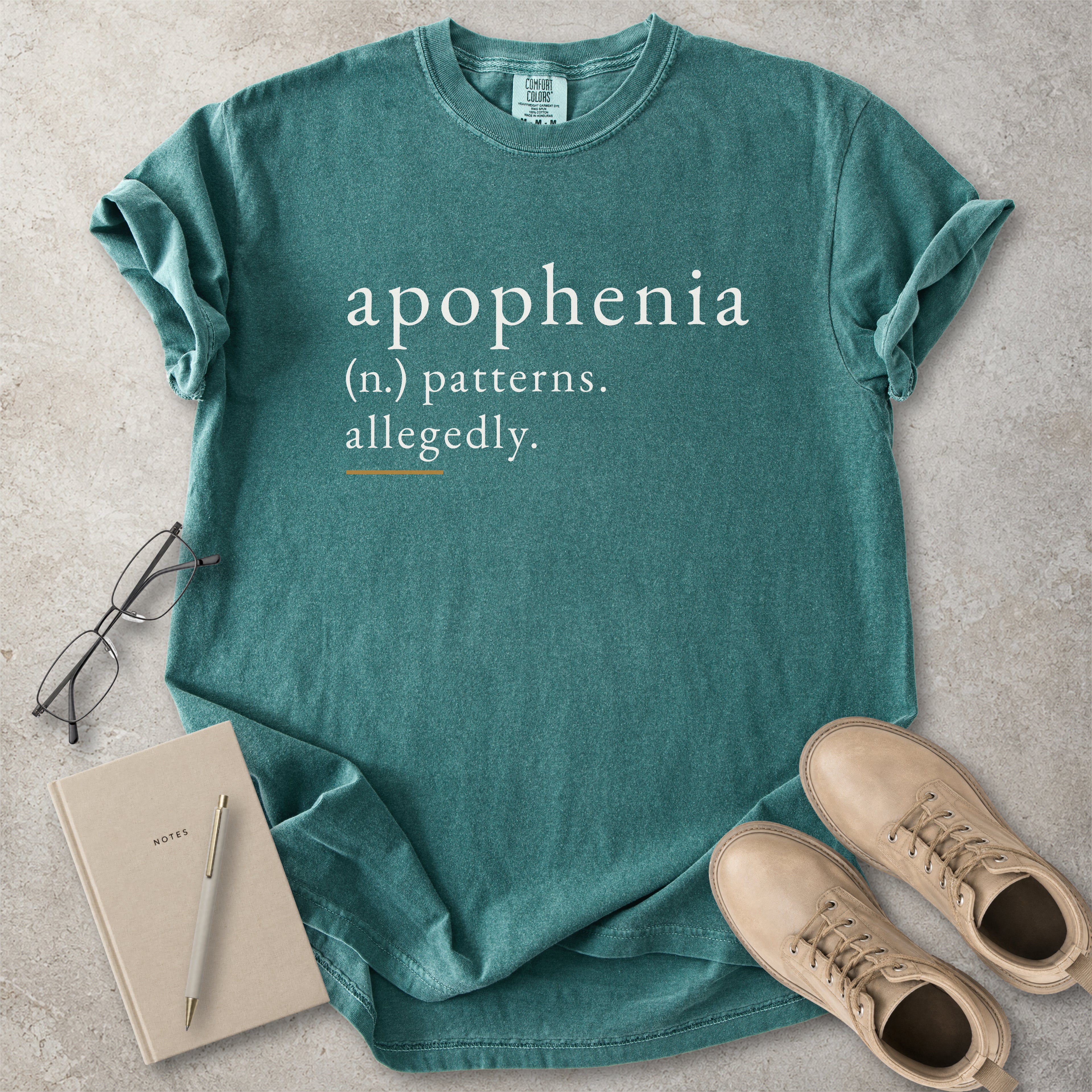 Blue spruce Comfort Colors graphic T-shirt with apophenia definition text reading patterns allegedly, styled with notebook, pen, glasses and tan boots