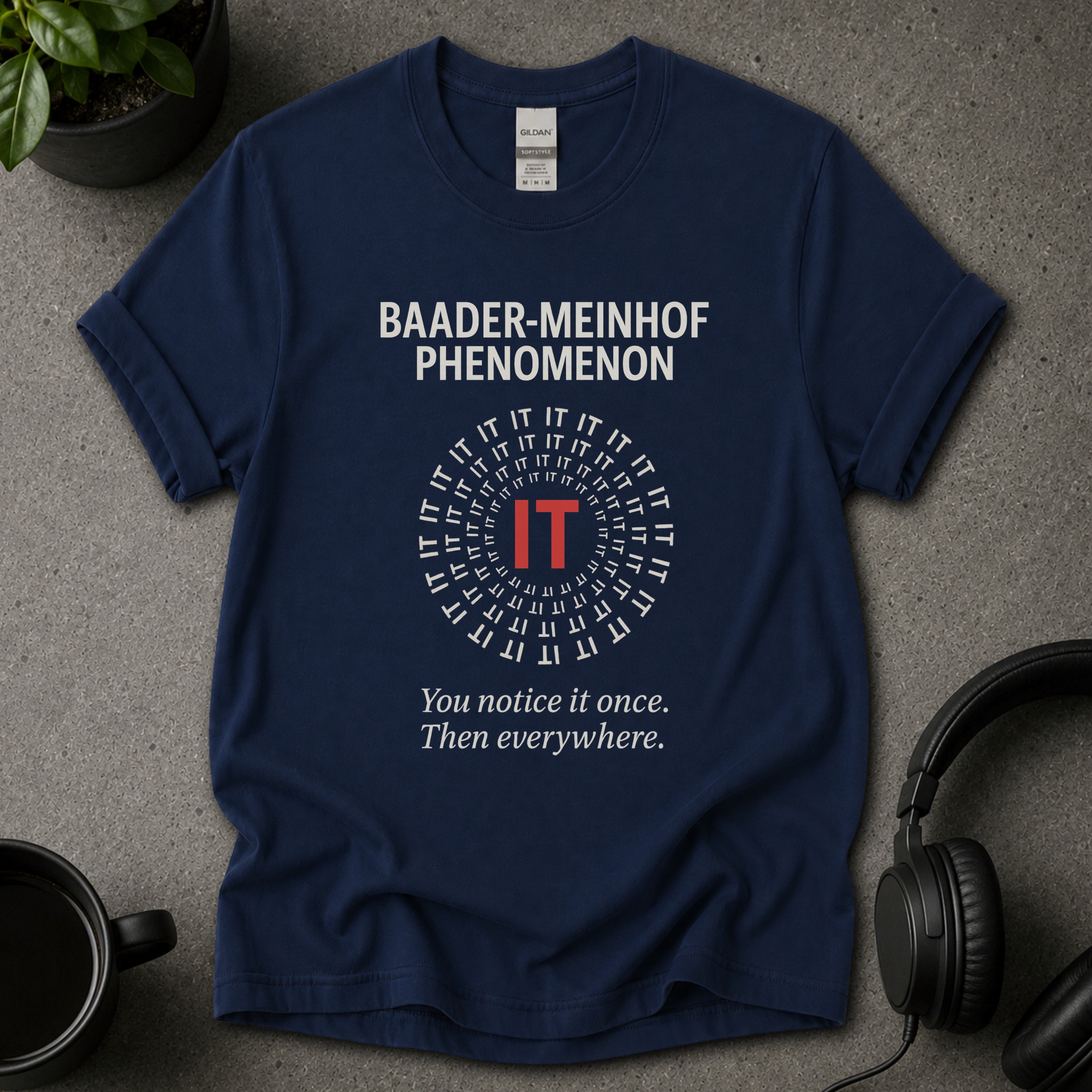 Navy blue t-shirt with 'Baader-Meinhof Phenomenon' text on a gray surface with headphones and a mug.