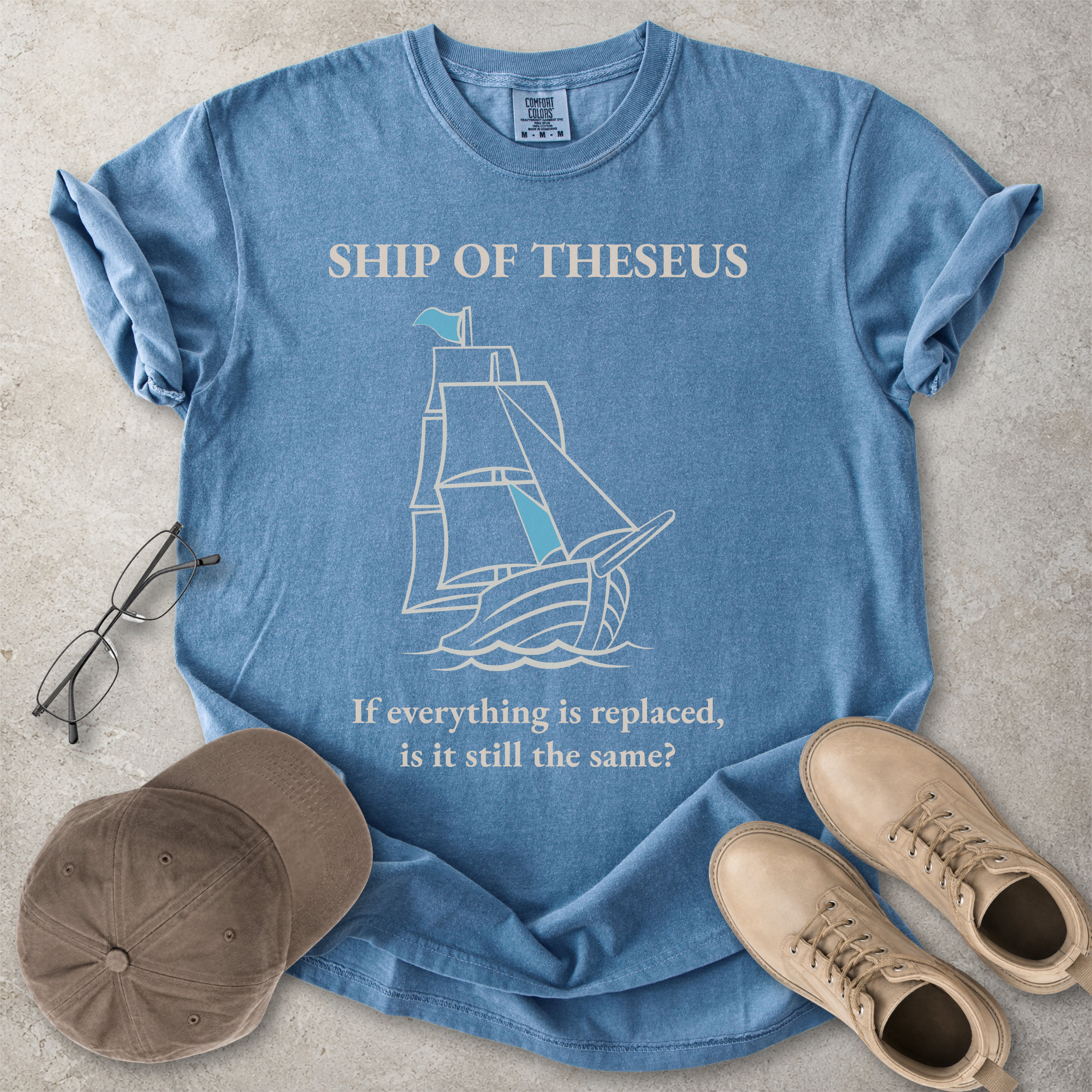 Blue jean Comfort Colors graphic T-shirt with Ship of Theseus text, line-art sailing ship and the phrase if everything is replaced is it still the same
