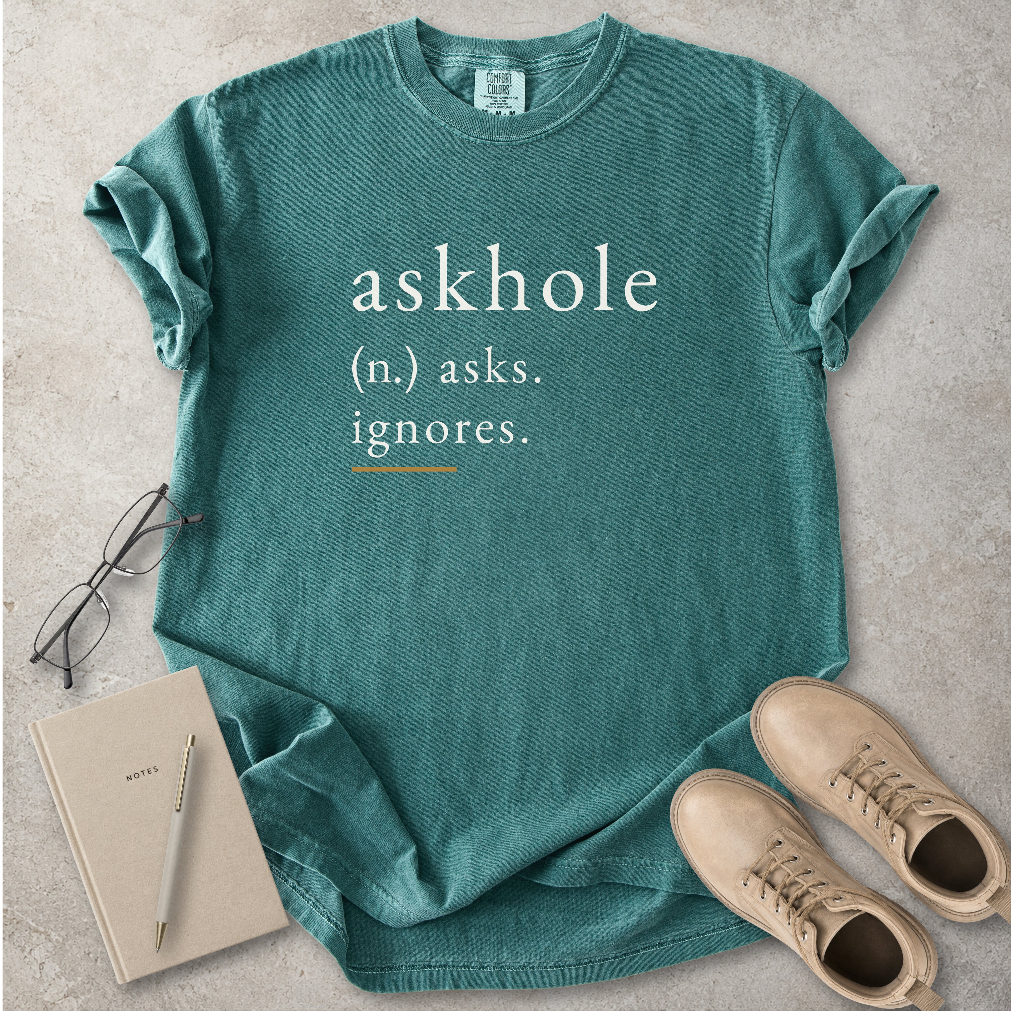 Blue spruce Comfort Colors graphic T-shirt with askhole definition text reading asks ignores, styled with notebook, pen, glasses and tan boots