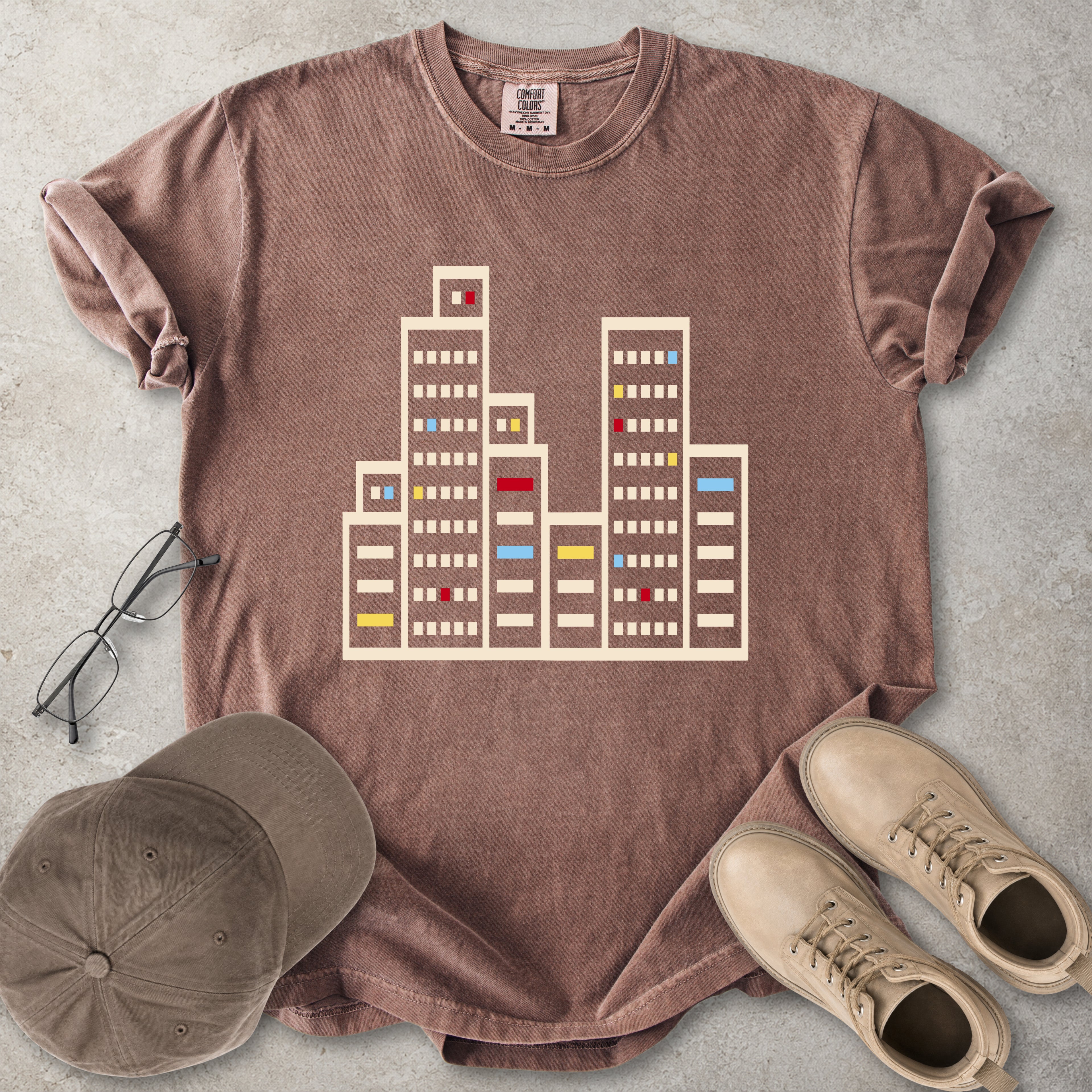 Espresso brown Comfort Colors graphic T-shirt with a minimalist cityscape window design, styled with glasses, cap and tan boots