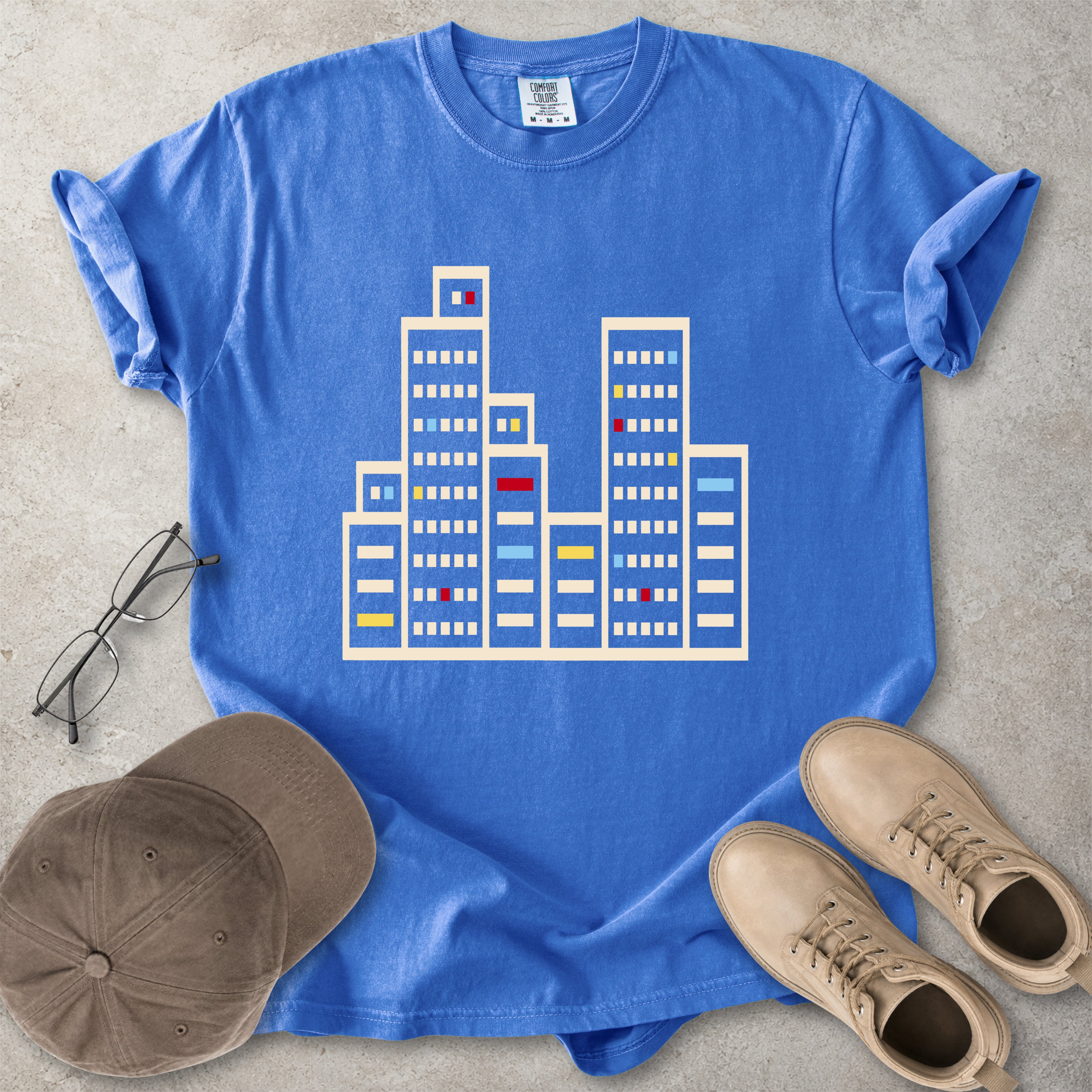 Flo blue Comfort Colors graphic T-shirt with a minimalist cityscape window design, styled with glasses, cap and tan boots