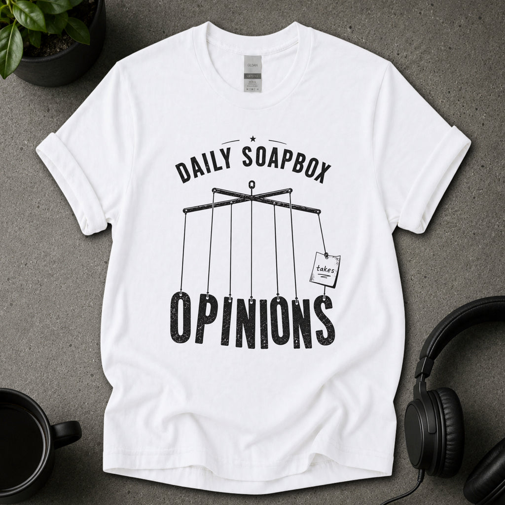 White t-shirt with 'Daily Soapbox Opinions' graphic on a gray surface with a mug and headphones.