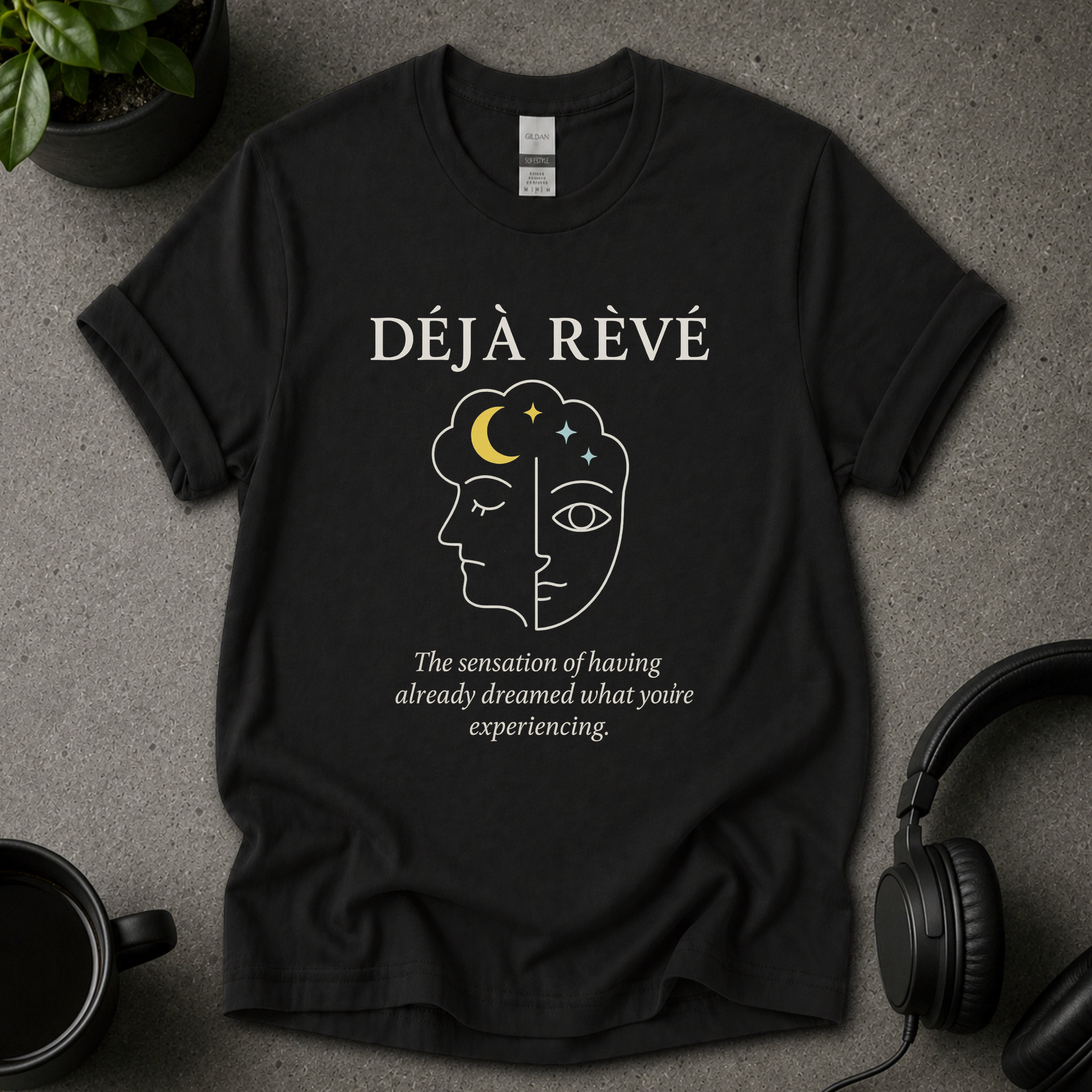 Black t-shirt with 'Déj  Rèvé' design on a gray surface with a cup and headphones.