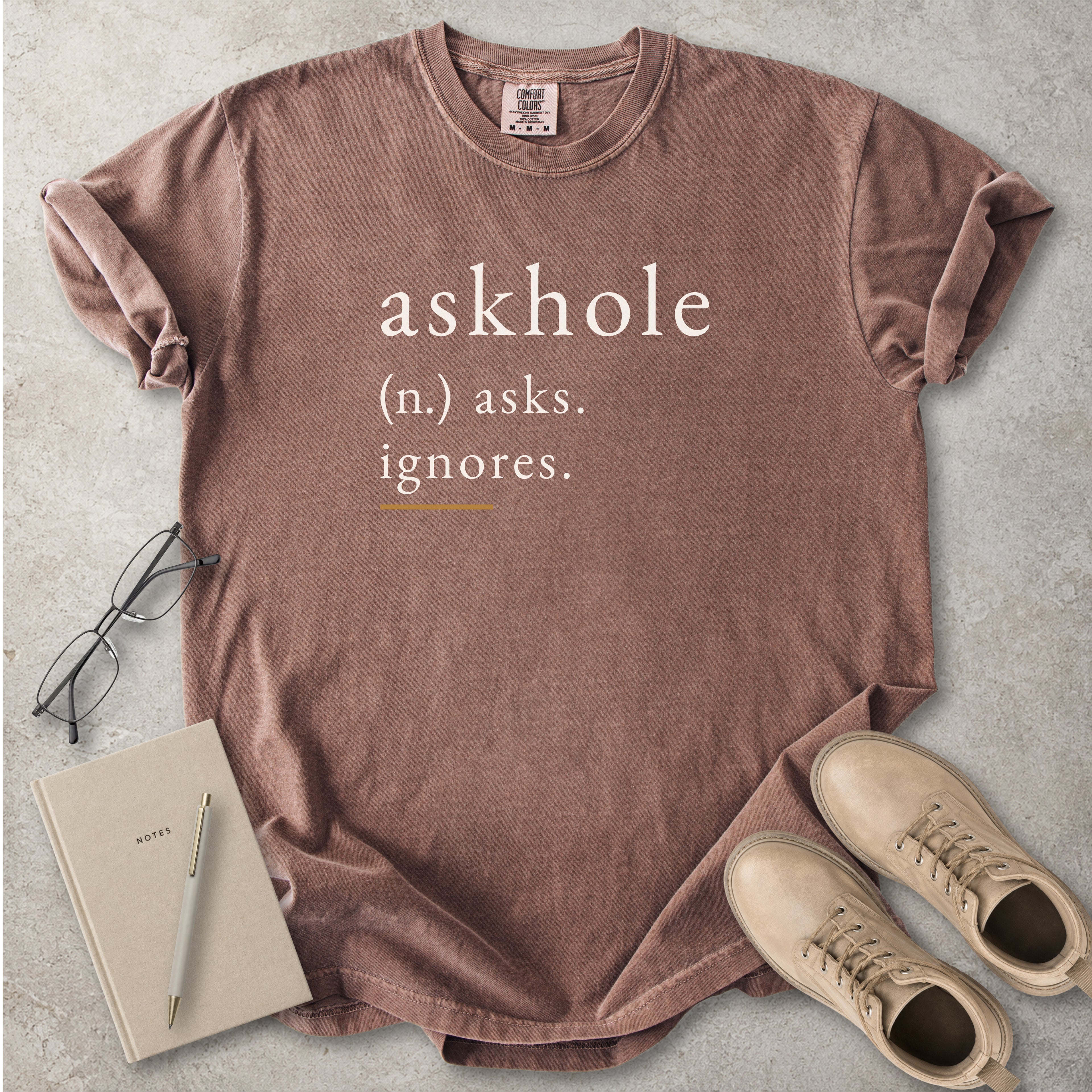Espresso brown Comfort Colors graphic T-shirt with askhole definition text reading asks ignores, styled with notebook, pen, glasses and tan boots