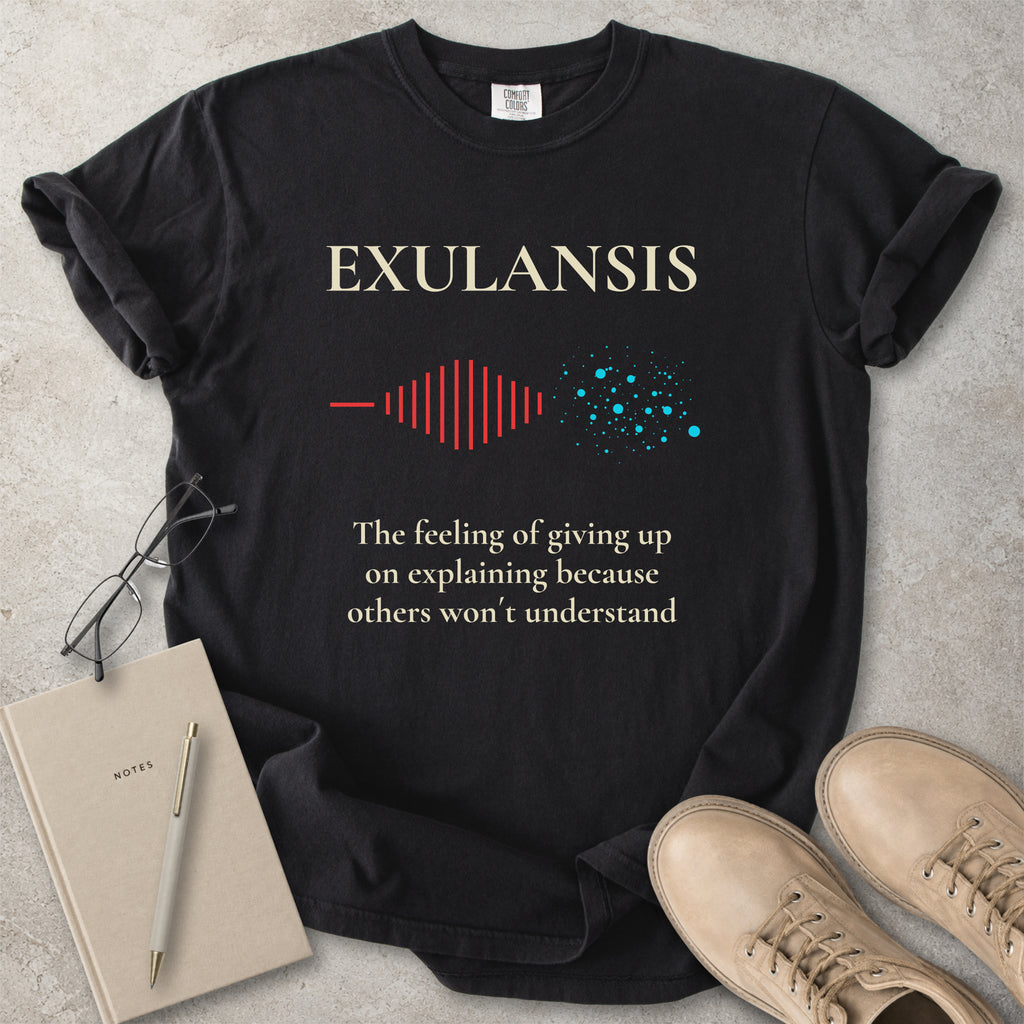 Black t-shirt with 'EXULANSIS' text and graphics on a concrete surface with glasses, notebook, and shoes.