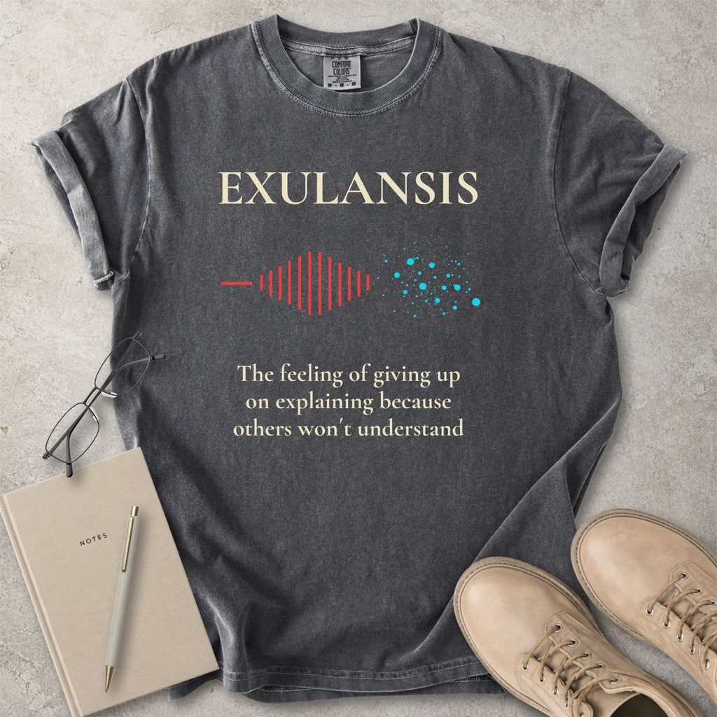 Gray t-shirt with 'Exulansis' design and text on a concrete surface with a notebook and shoes.