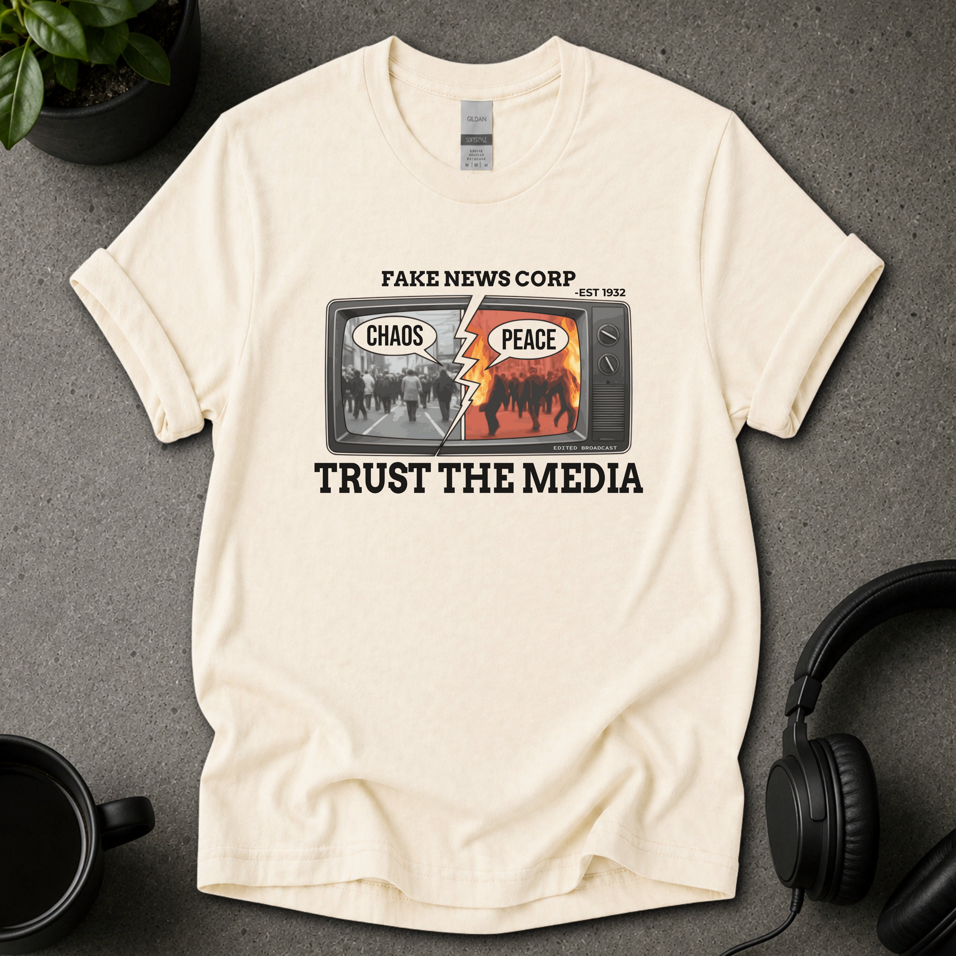 Beige t-shirt with graphic design and text on a gray surface with a plant and mug in the background