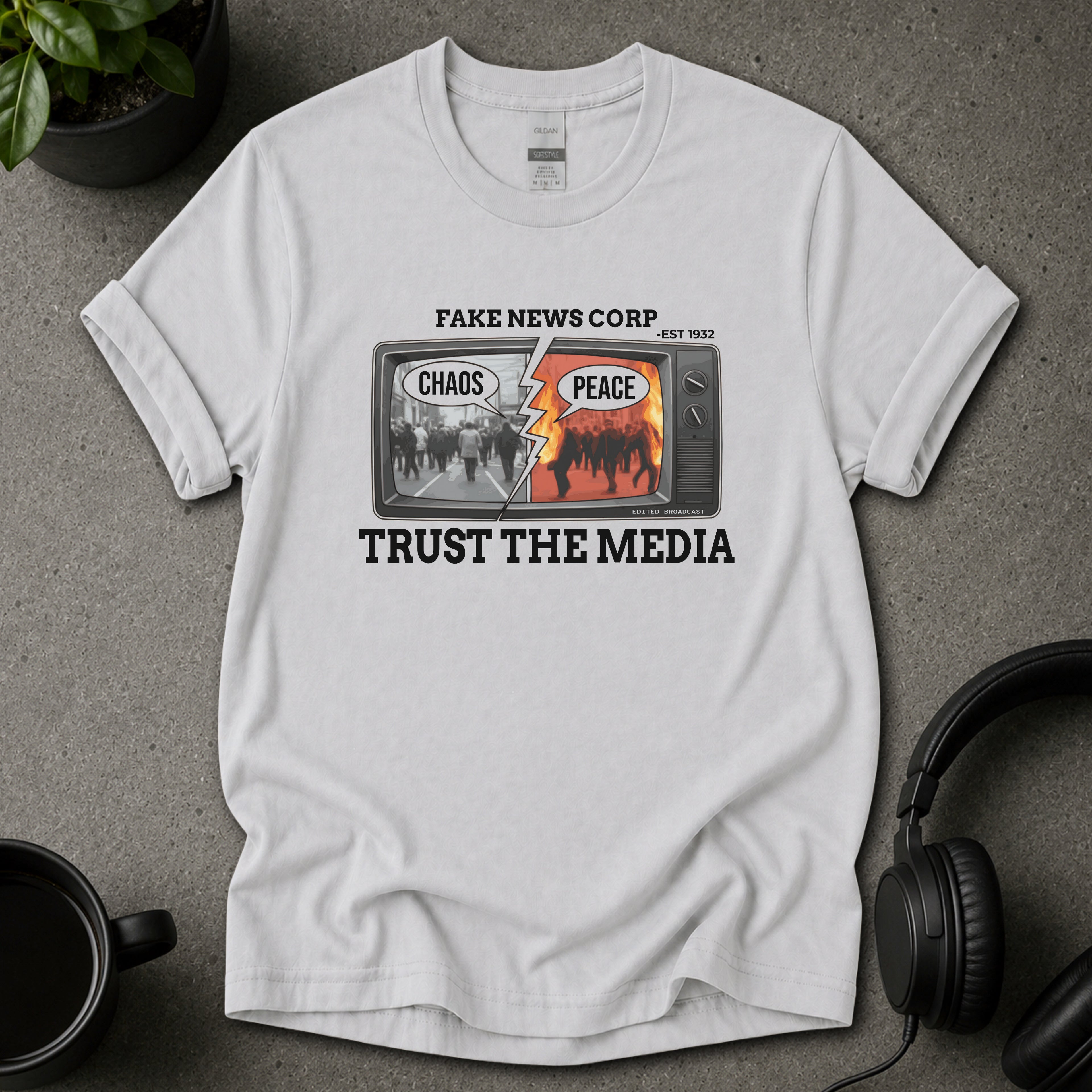 White t-shirt with graphic design and text on a gray surface with headphones and a plant.
