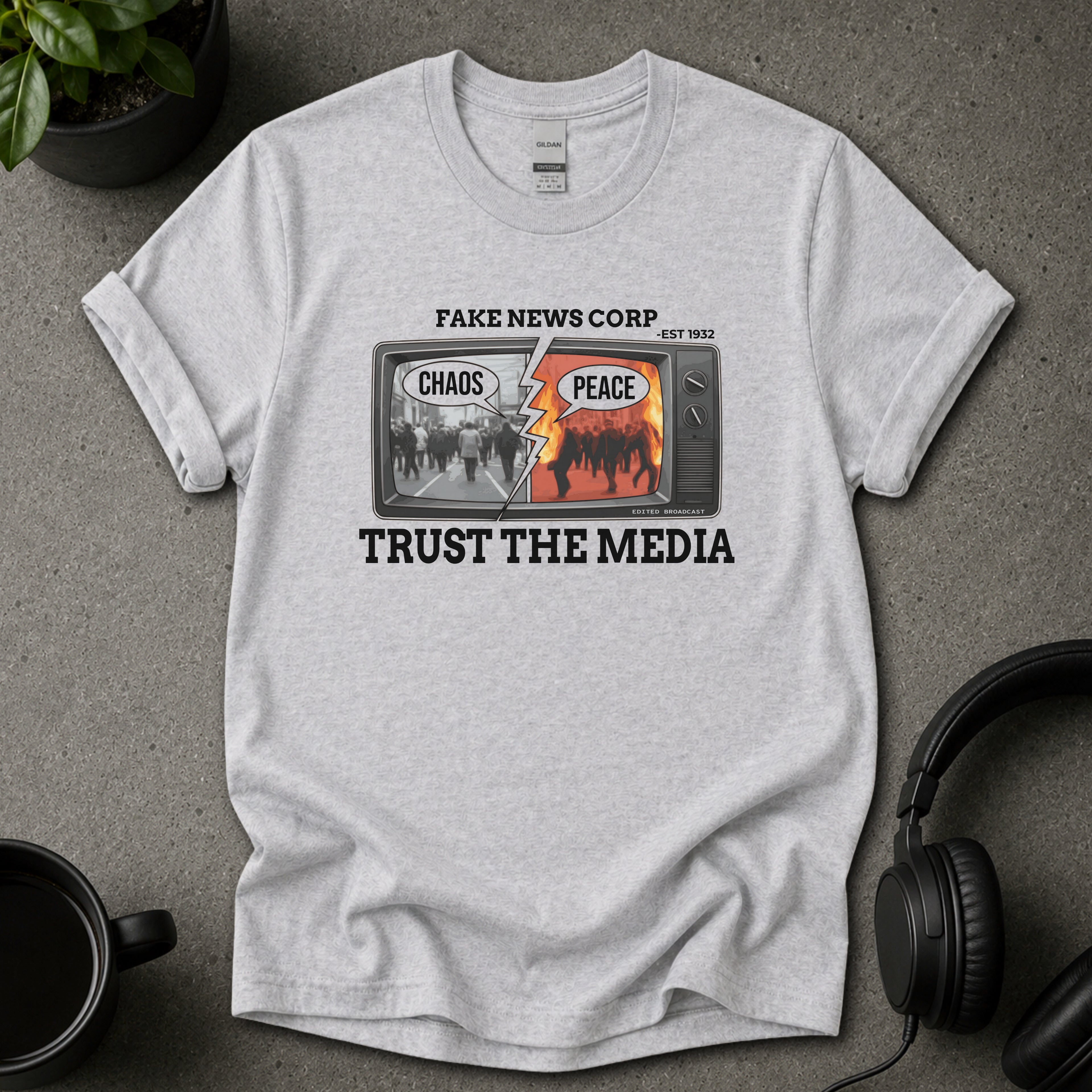 Gray t-shirt with graphic design and text on a gray surface with a plant and headphones.