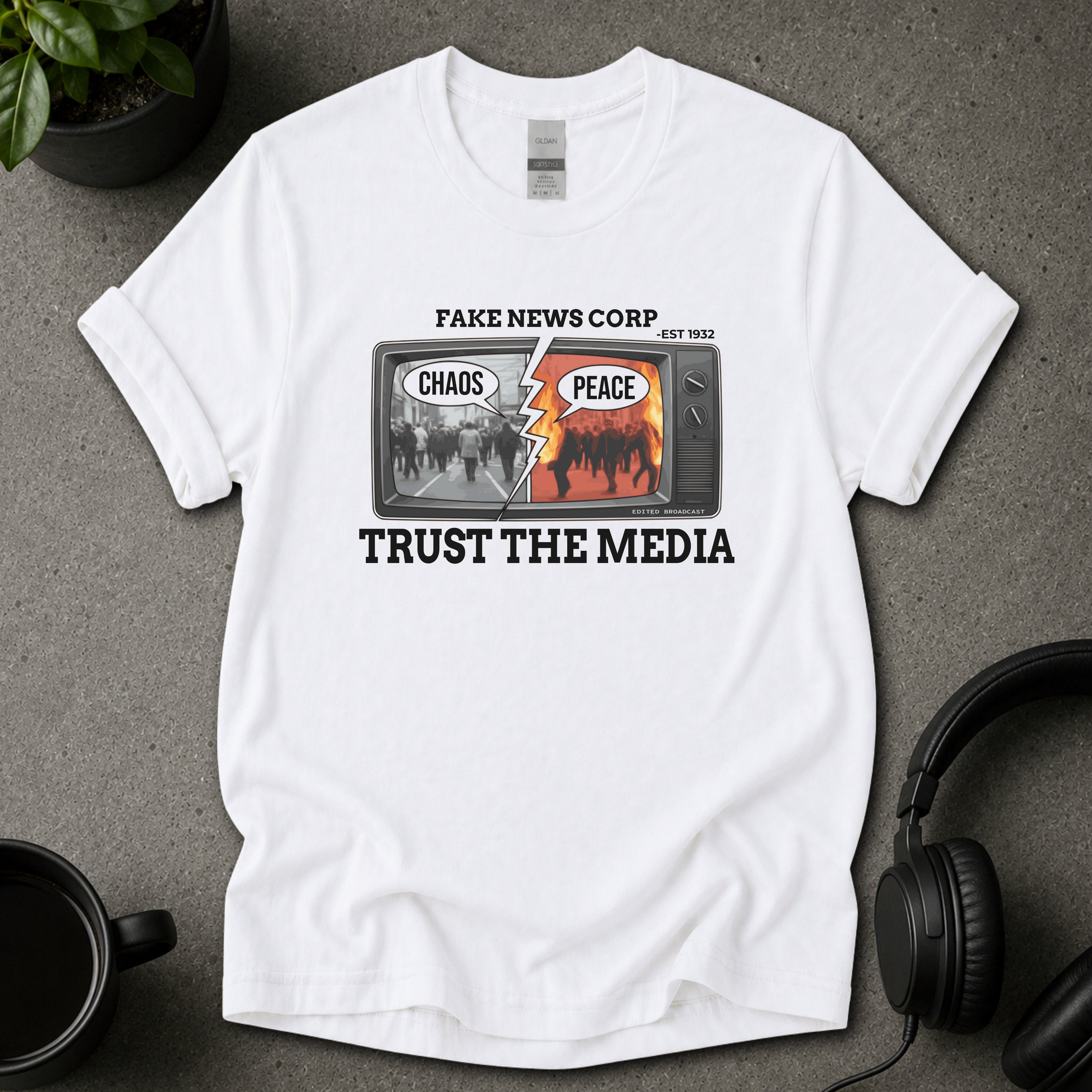 White t-shirt with Fake news corp anti media graphic tee white design and text on a gray surface with headphones and a mug.