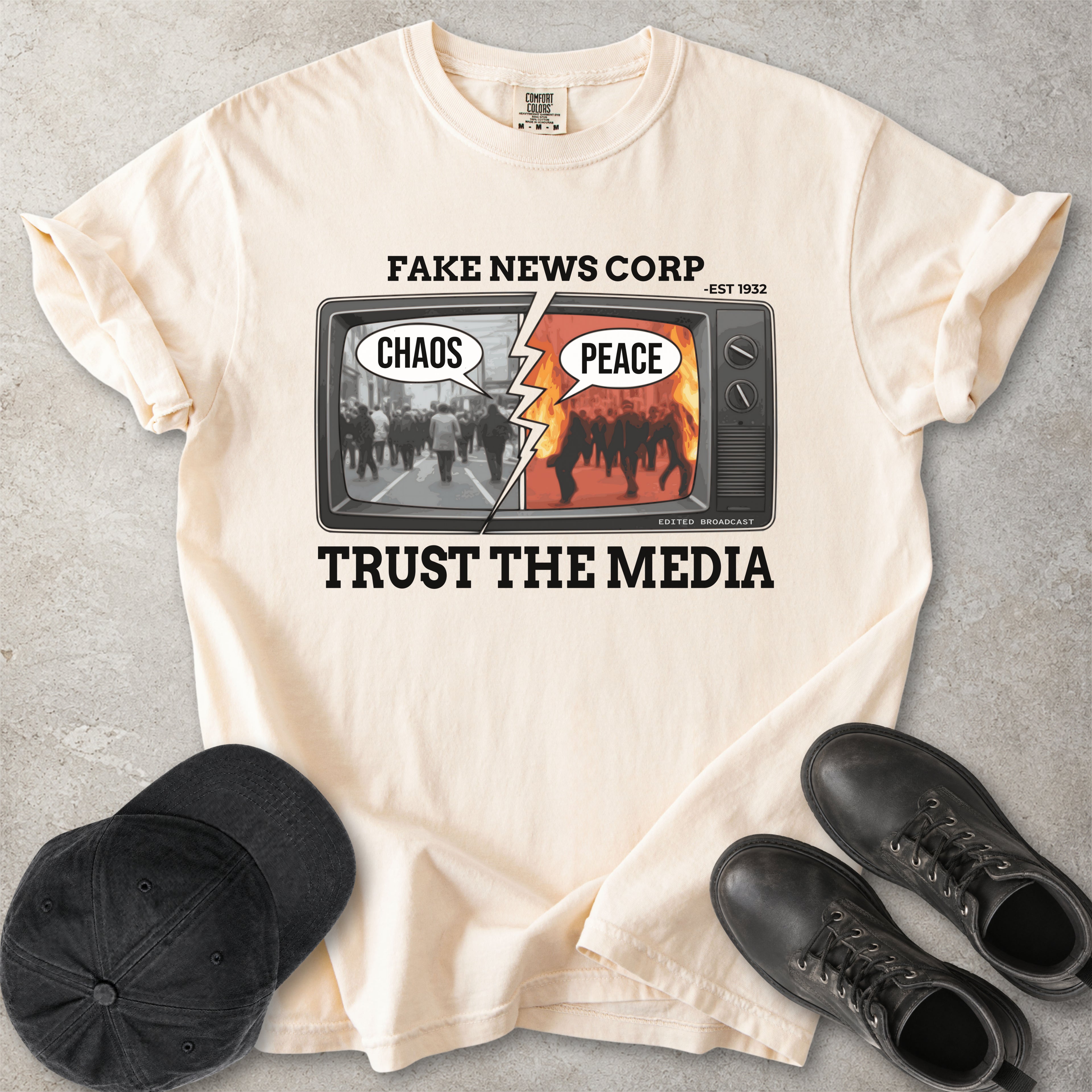Ivory beige Comfort Colors graphic T-shirt with Fake News Corp trust the media TV design showing chaos and peace screens, styled with black cap and boots