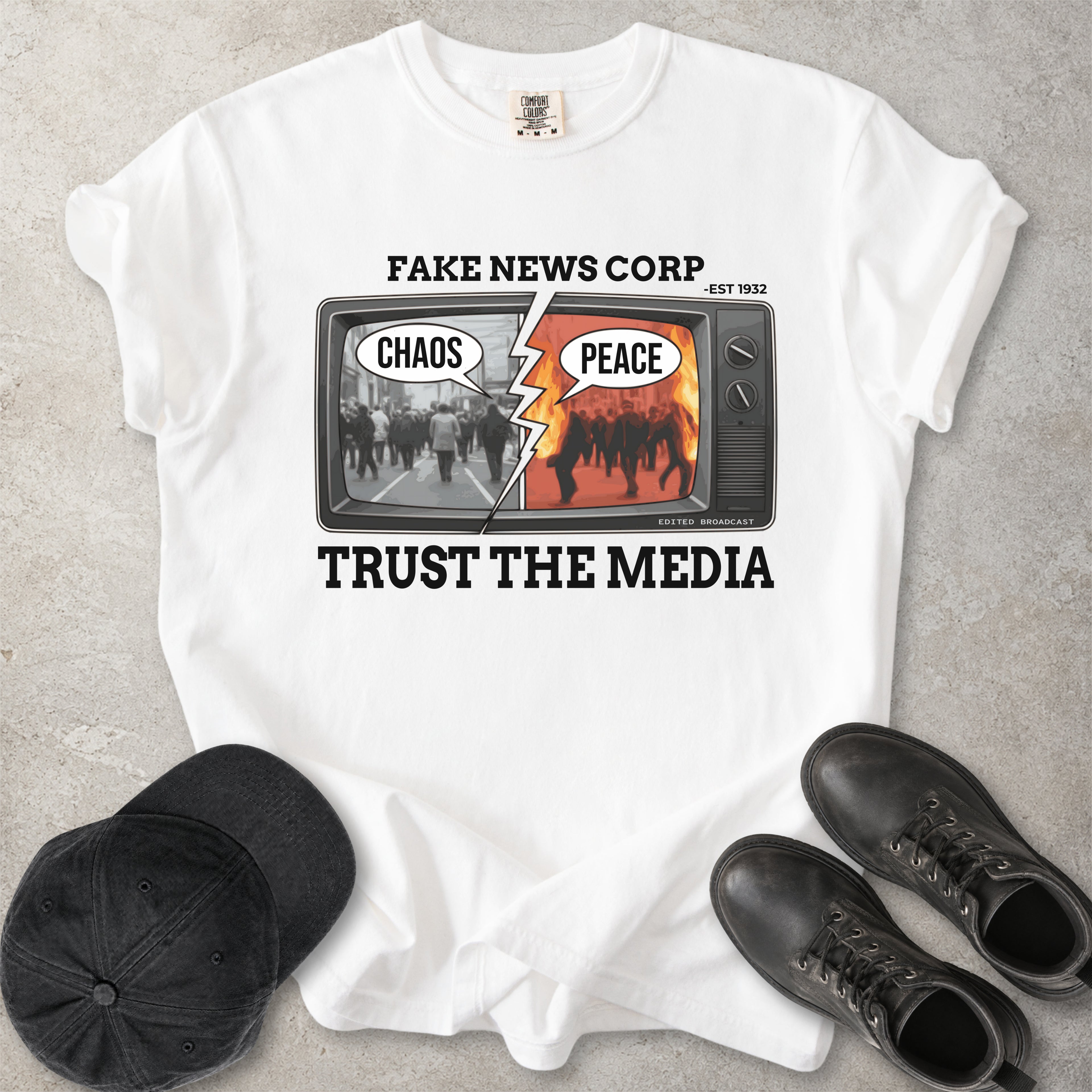 White Comfort Colors graphic T-shirt with Fake News Corp trust the media TV design showing chaos and peace screens, styled with black cap and boots