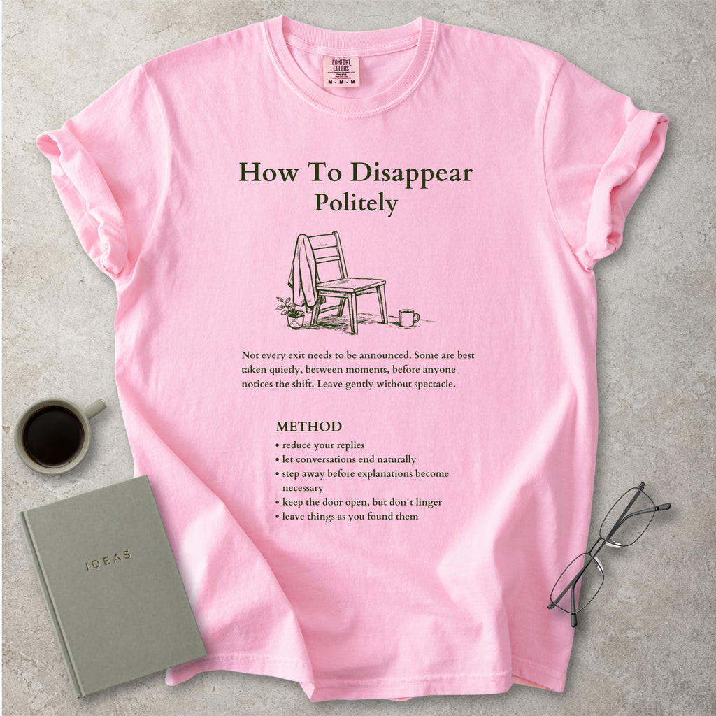 Pink Comfort Colors graphic T-shirt with green How To Disappear Politely design, chair illustration and quiet exit method text, styled with coffee, notebook and glasses