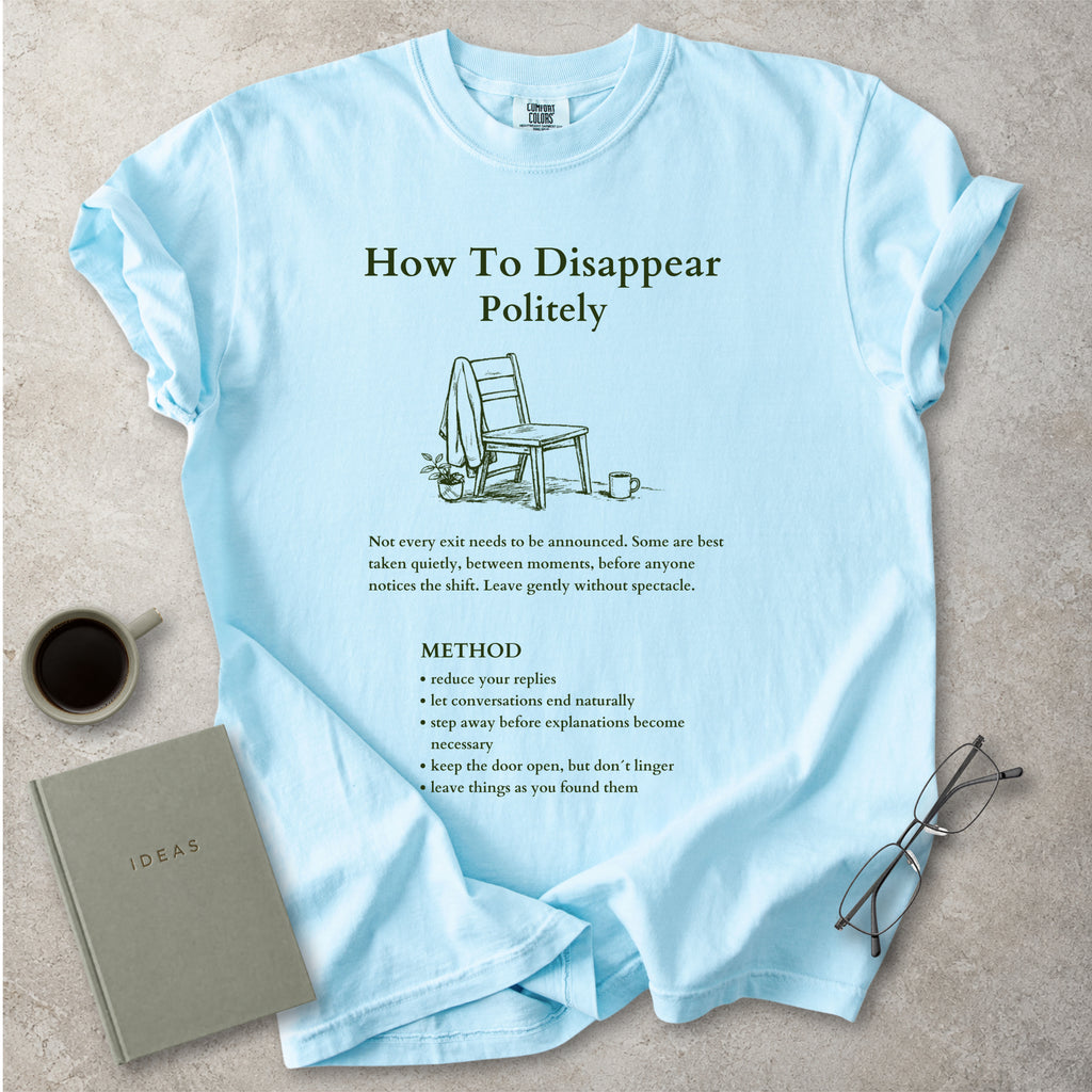 Light blue Comfort Colors graphic T-shirt with green How To Disappear Politely design, chair illustration and quiet exit method text, styled with coffee, notebook and glasses