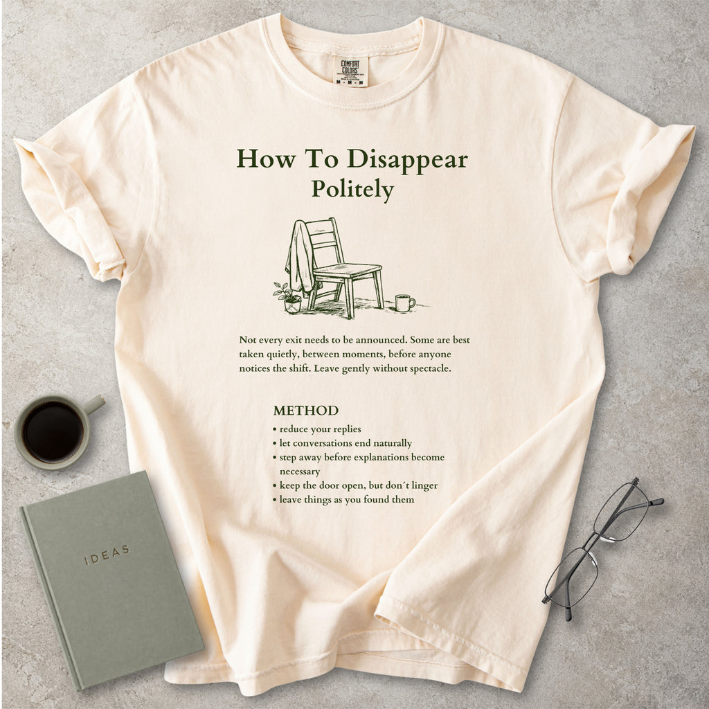 Beige Comfort Colors graphic T-shirt with green How To Disappear Politely design, chair illustration and quiet exit method text, styled with coffee, notebook and glasses