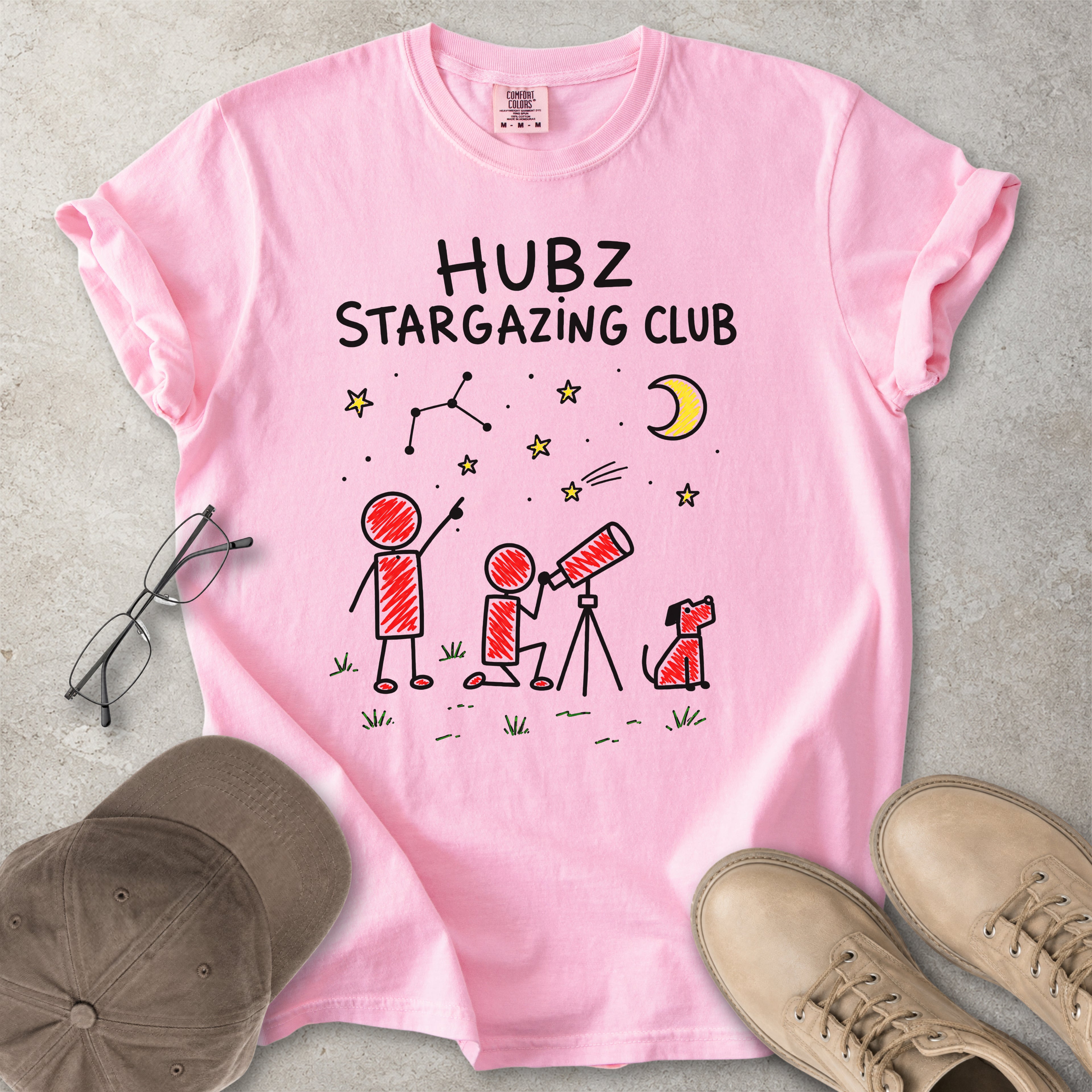 Pink t-shirt with 'HUBZ Stargazing Club' design on a gray surface with accessories.